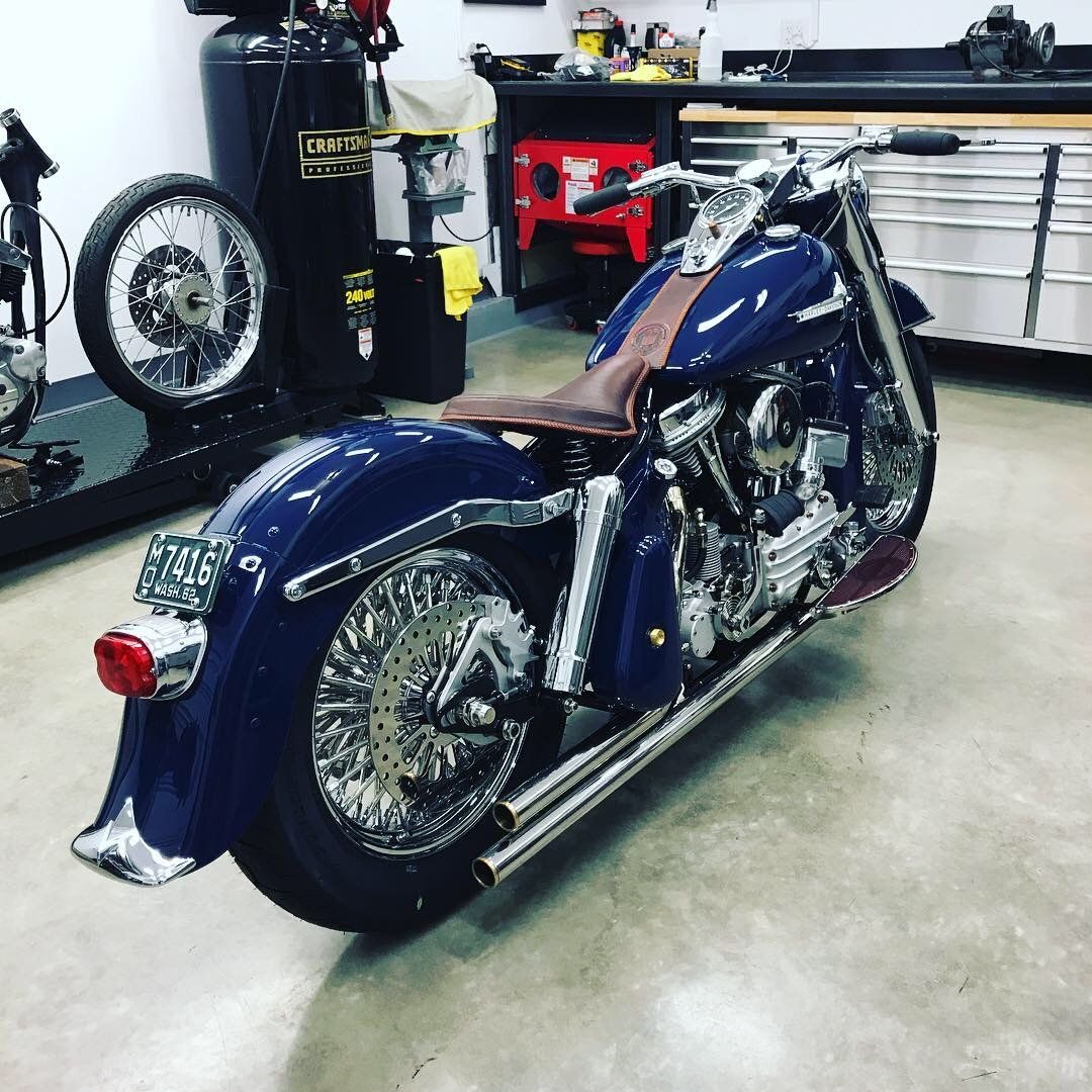 Blue custom motorcycle in a garage workshop, with chrome details and a brown leather seat.