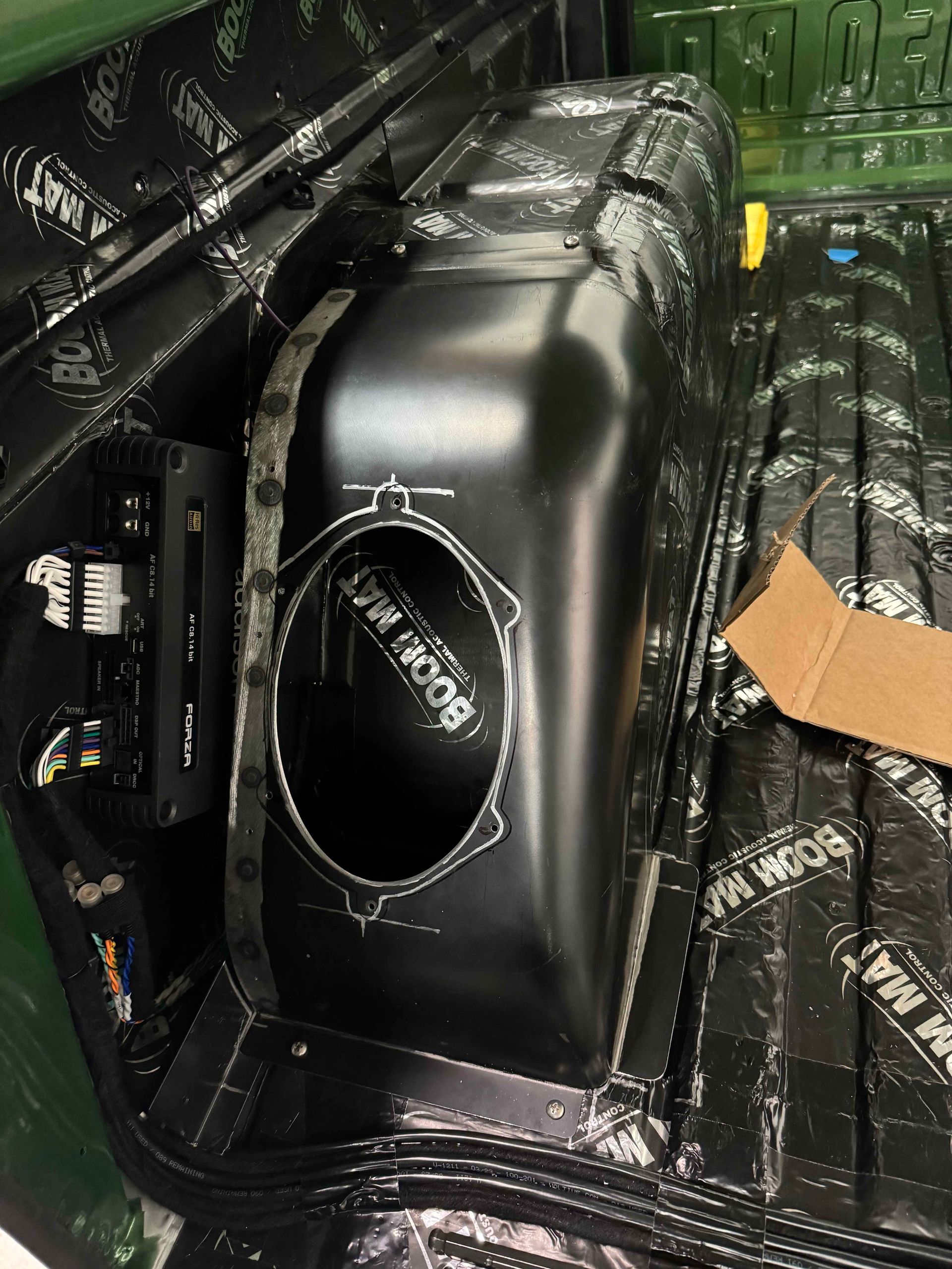 Black car audio subwoofer enclosure with a round speaker opening in a trunk.