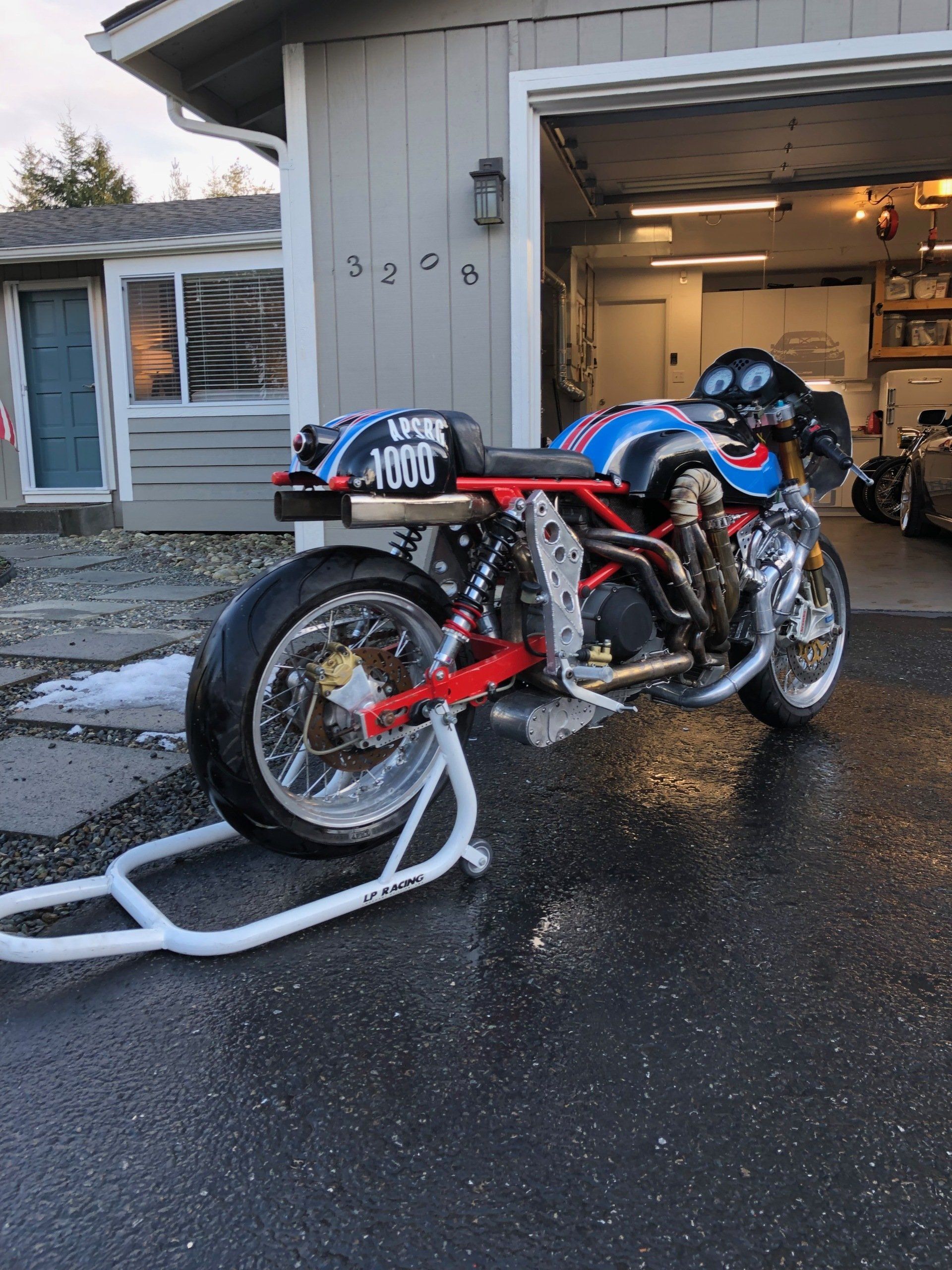 Blue and red racing motorcycle strapped on a trailer outside a garage on a wet driveway
