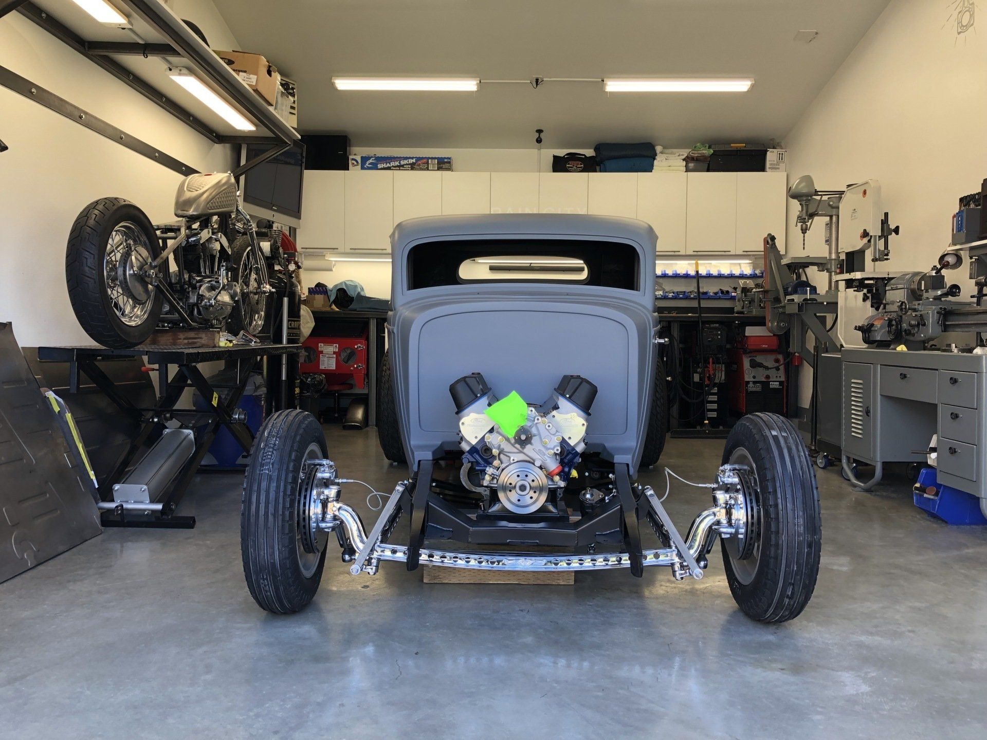 Custom hot rod car in a garage, front view with exposed engine and large front wheels.