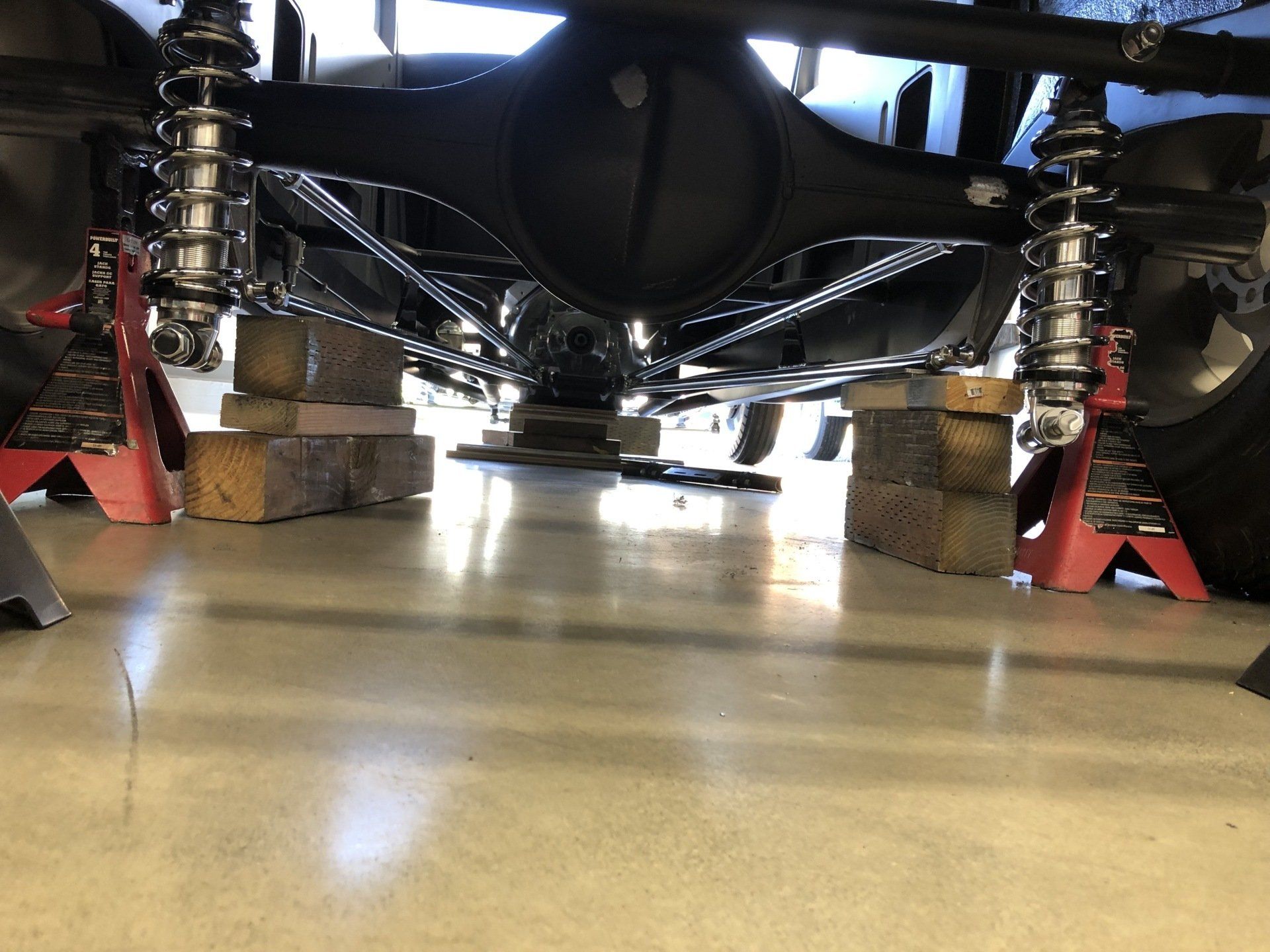 Low-angle view of a car’s suspension and undercarriage on blocks in a garage.