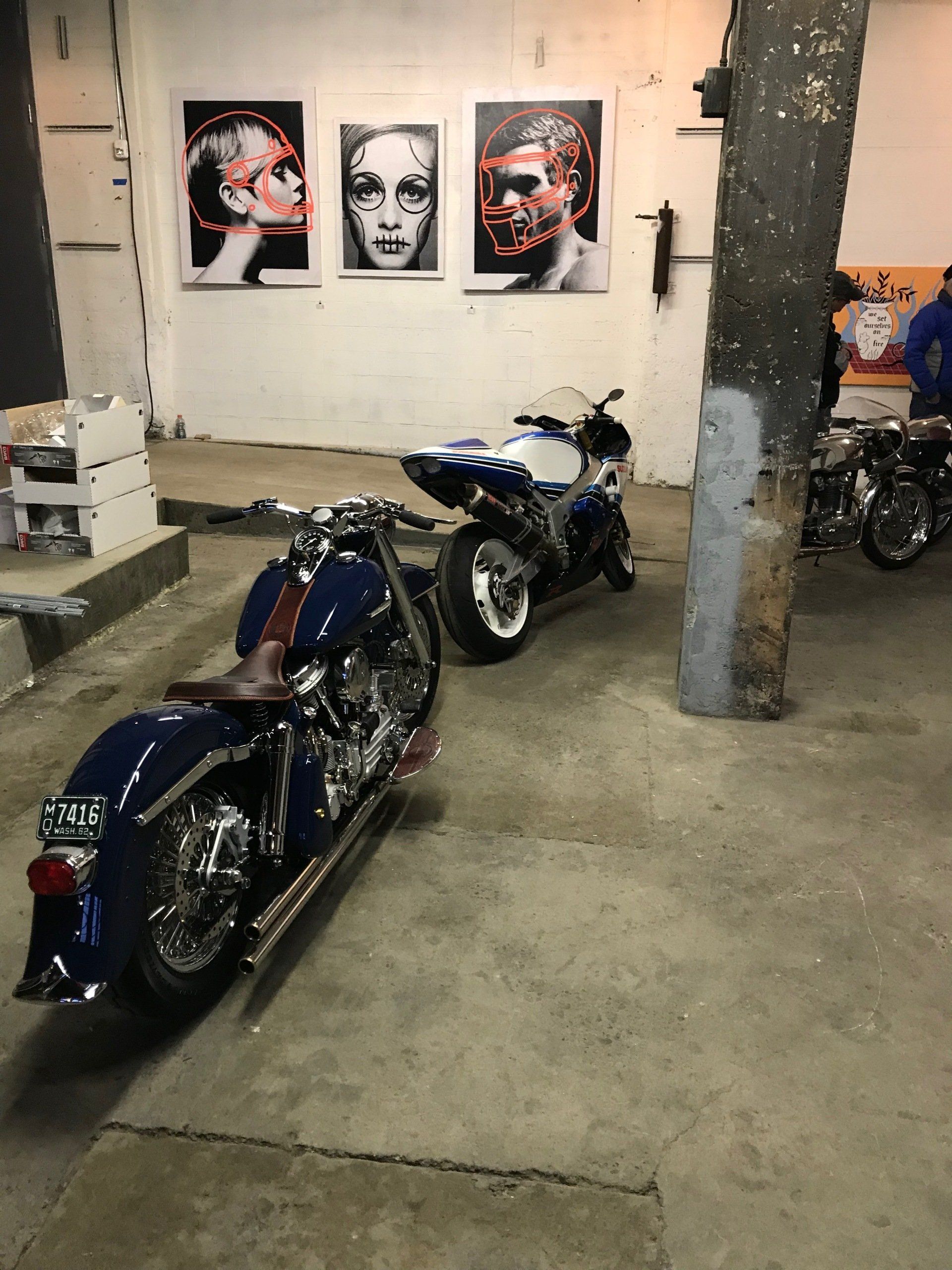 Three custom motorcycles parked in an indoor garage beneath three framed portraits on the wall