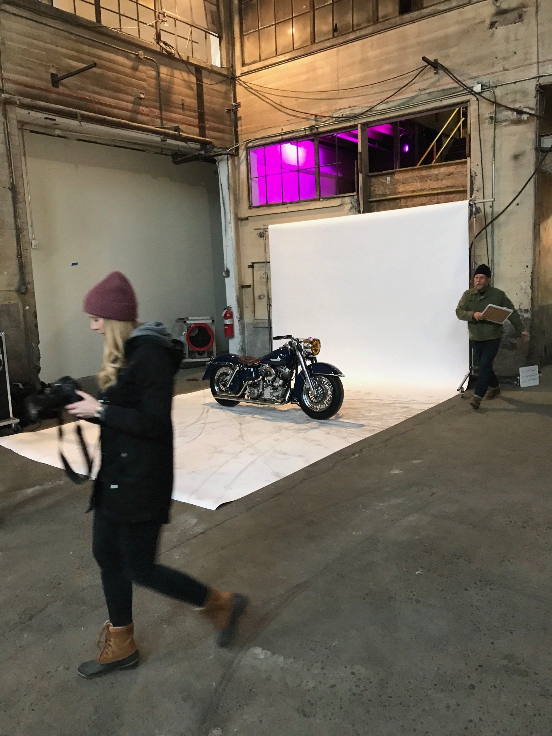Industrial studio with a motorcycle, bright white backdrop, and two people standing nearby.