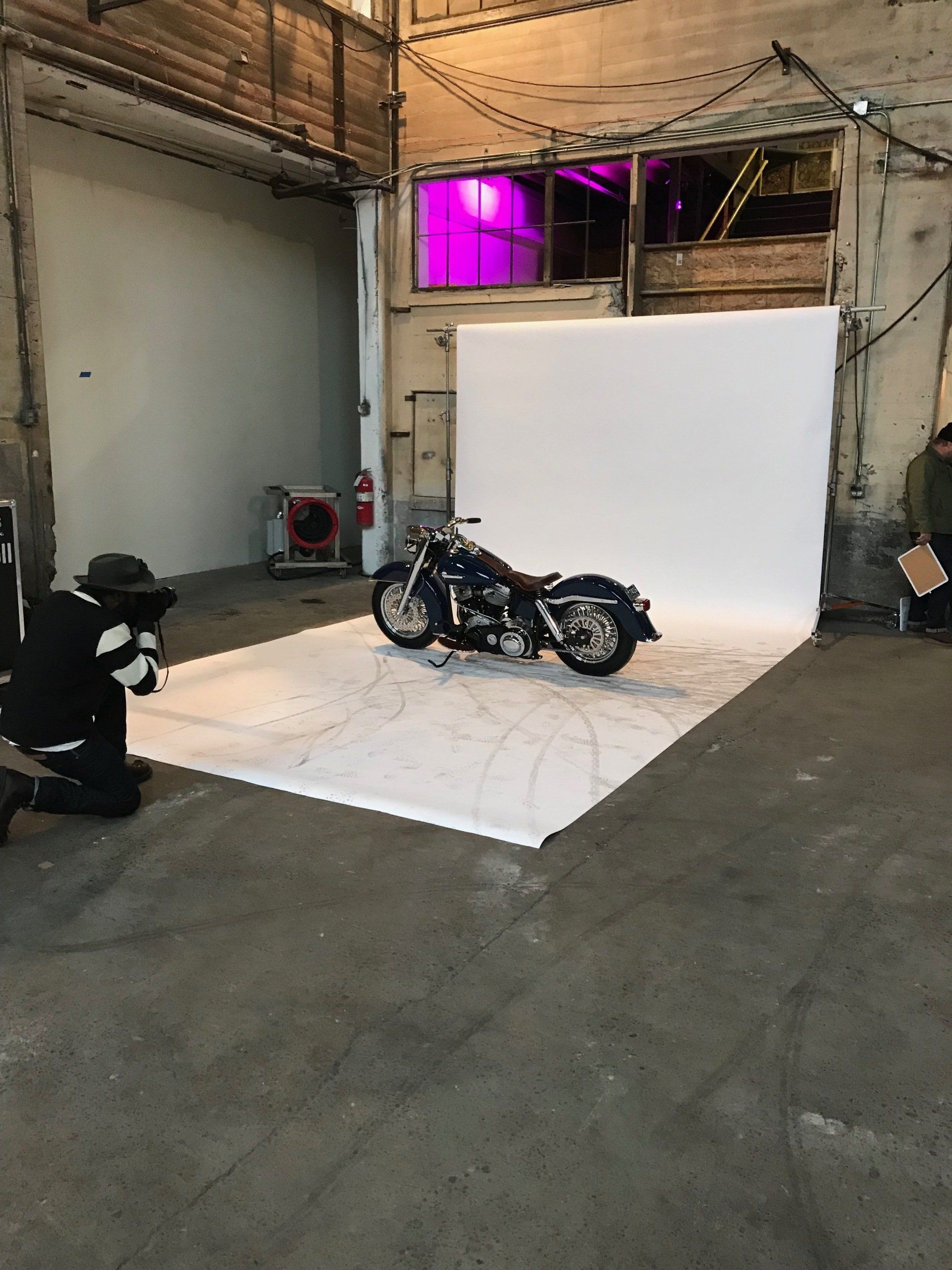 Motorcycle on a white backdrop in a warehouse studio, with purple lighting above.