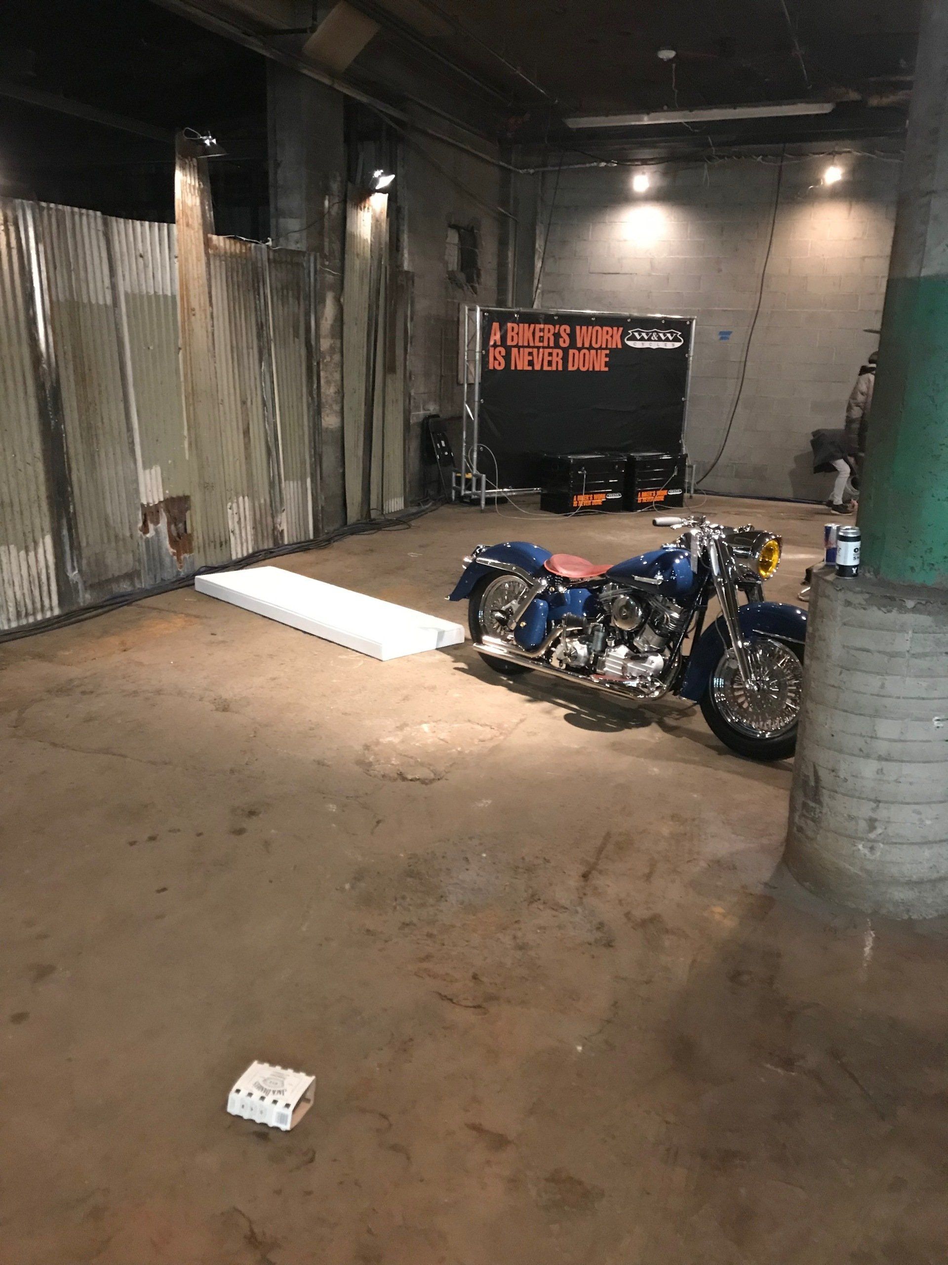 Motorcycle in a dim industrial garage with corrugated metal walls and a white board on the floor.