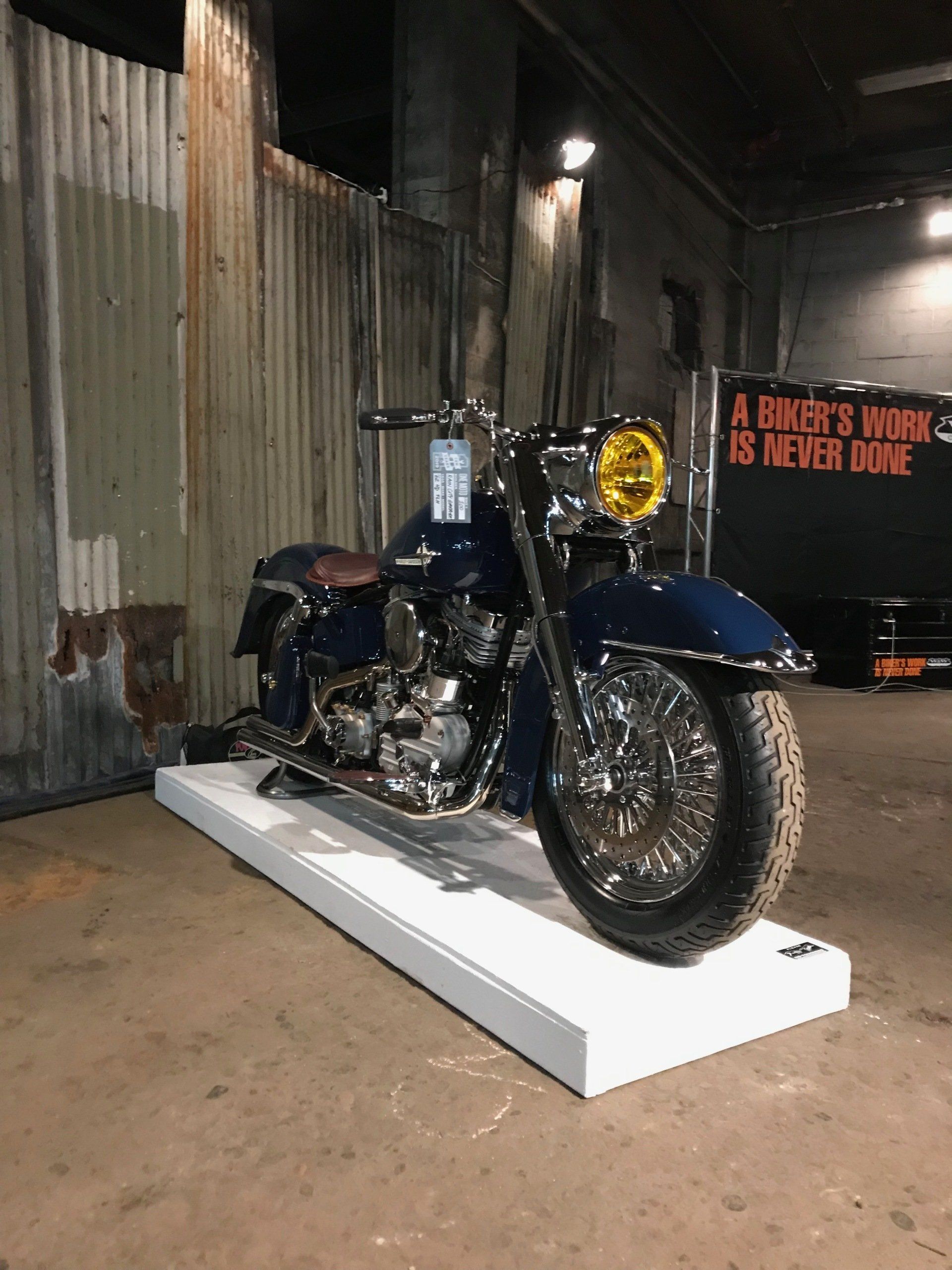 Blue motorcycle on a white display platform in an industrial alleyway.