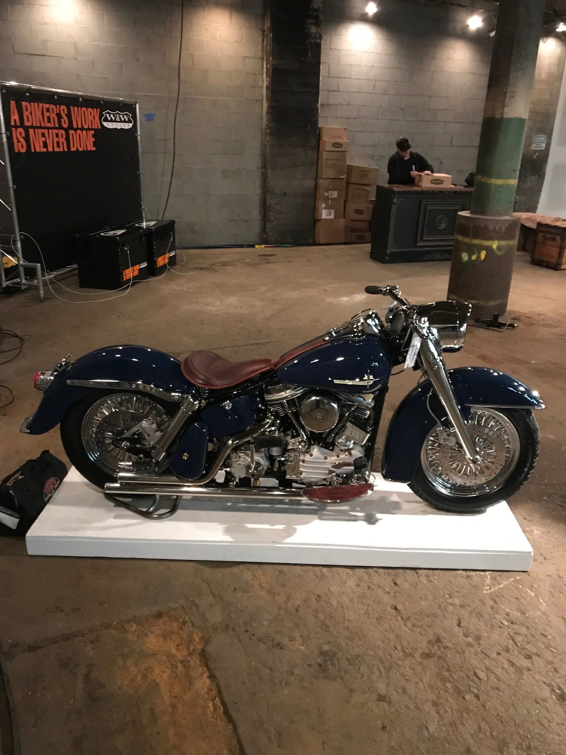 Blue-and-silver custom motorcycle on a white platform in an indoor event space