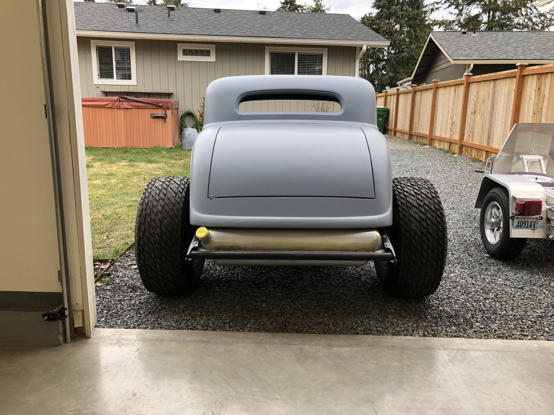 Gray hot rod car with large rear tires parked in a driveway, viewed from the garage opening.