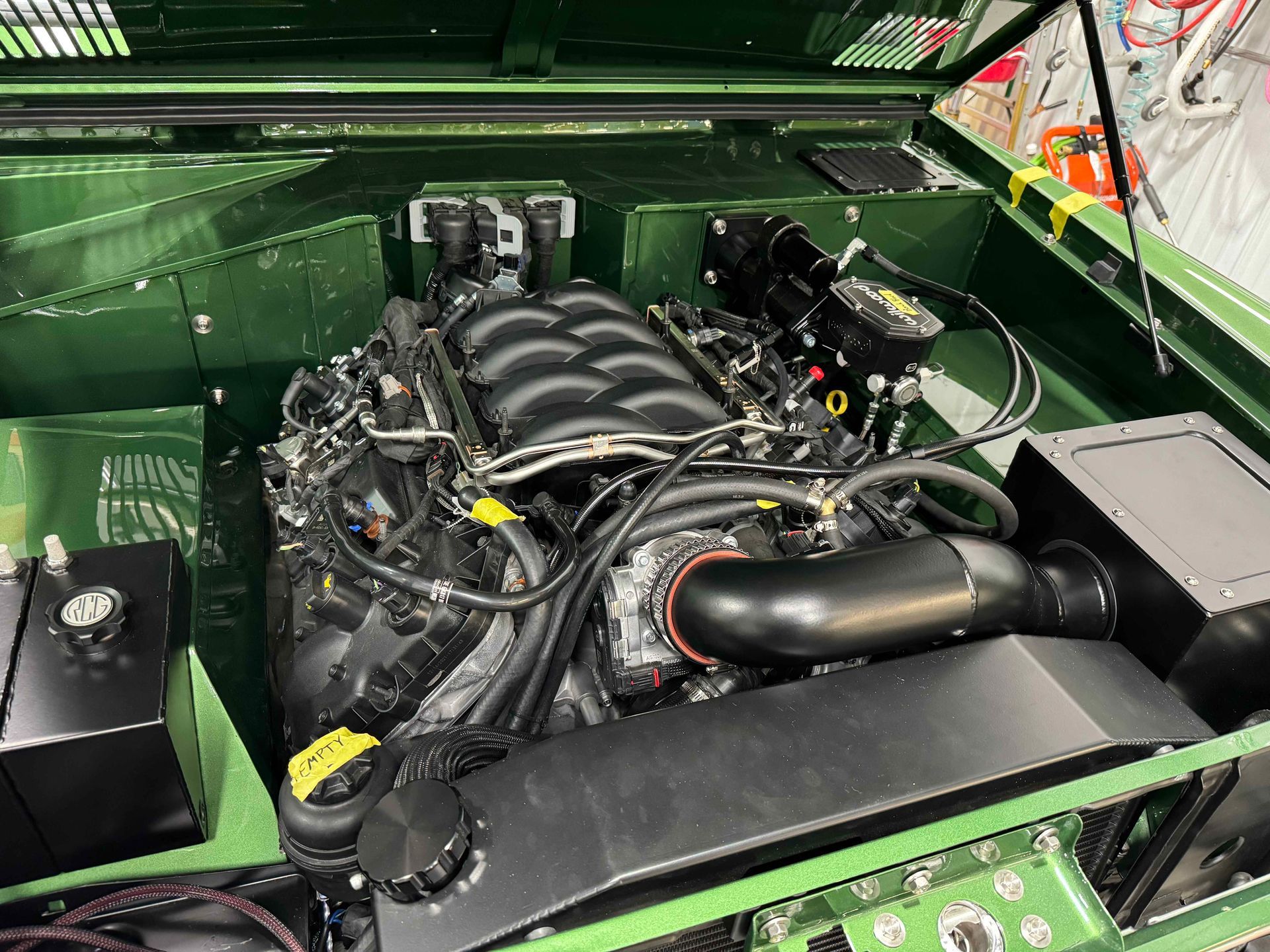 Green car engine bay with exposed V8 engine and black intake components