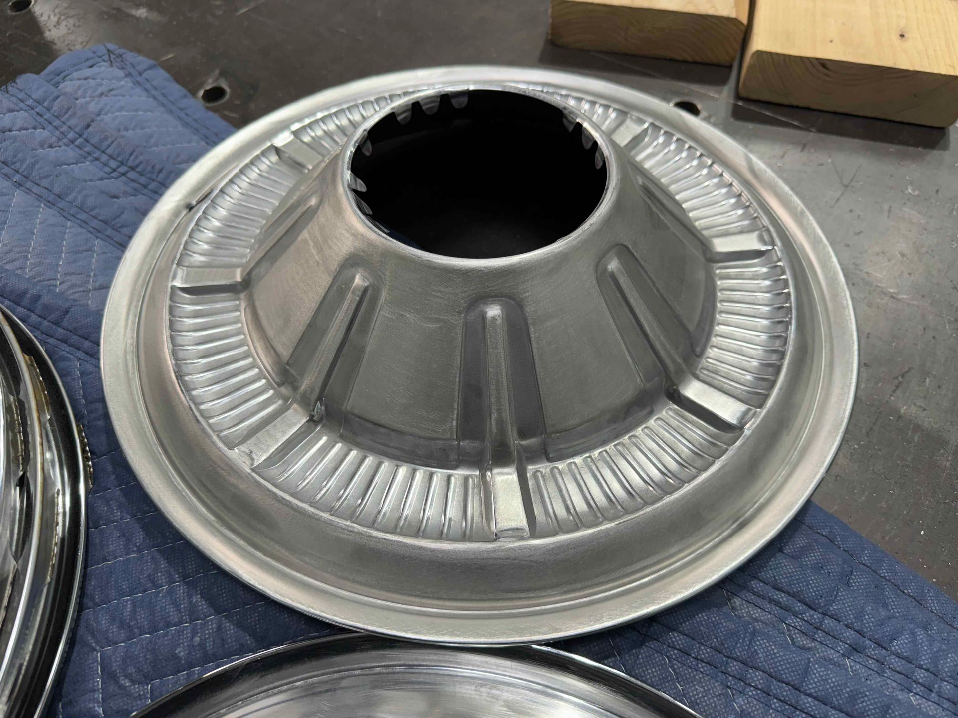 Metallic conical component with ribbed outer ring, resting on a blue cloth in a workshop setting
