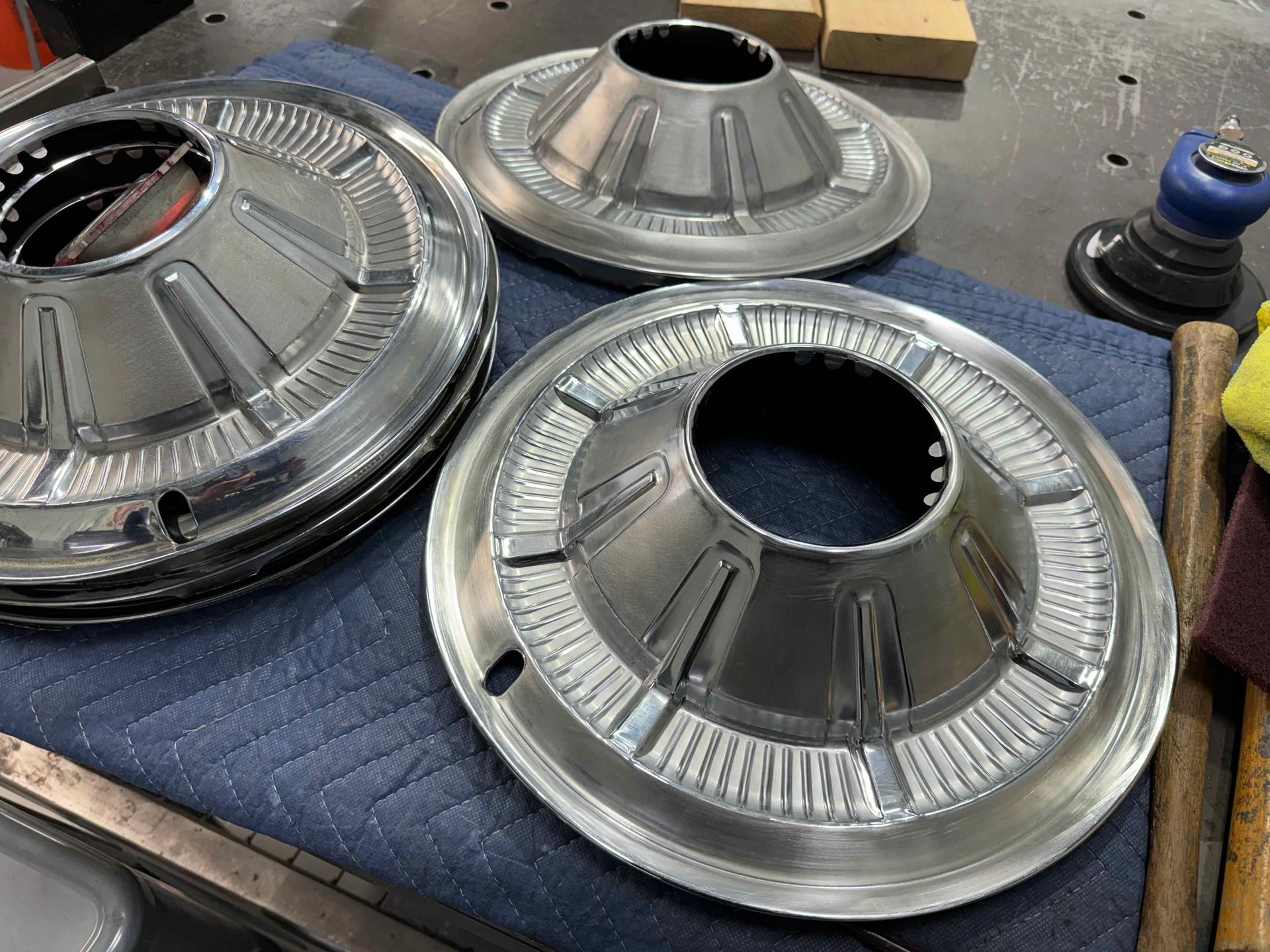 Three shiny metal automotive wheel hubcaps on a workbench, with tools nearby