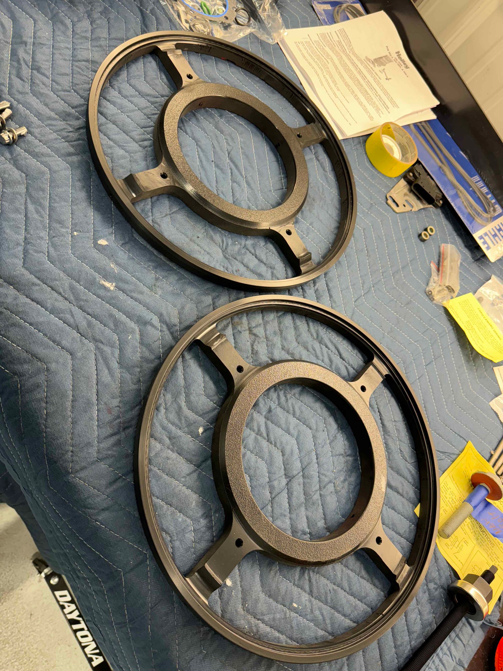 Two rusted metal steering wheels on a blue quilt, with papers and small tools nearby