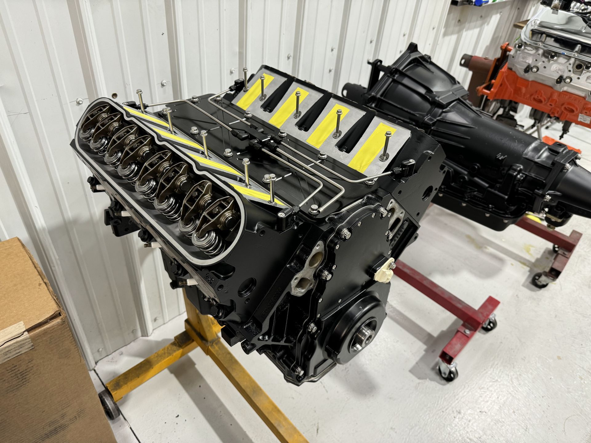 Black V8 engine on a stand in a workshop, with yellow straps and exposed valve covers.