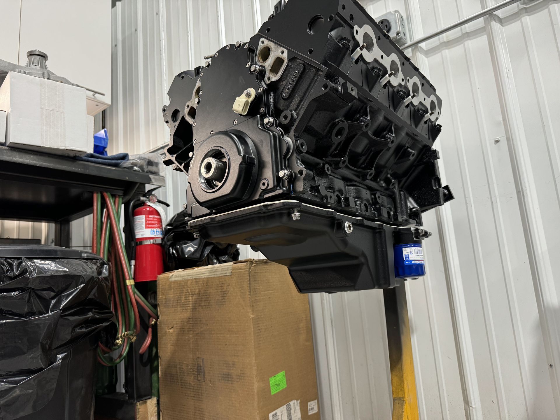 Black engine block mounted above a cardboard box in an industrial workshop.