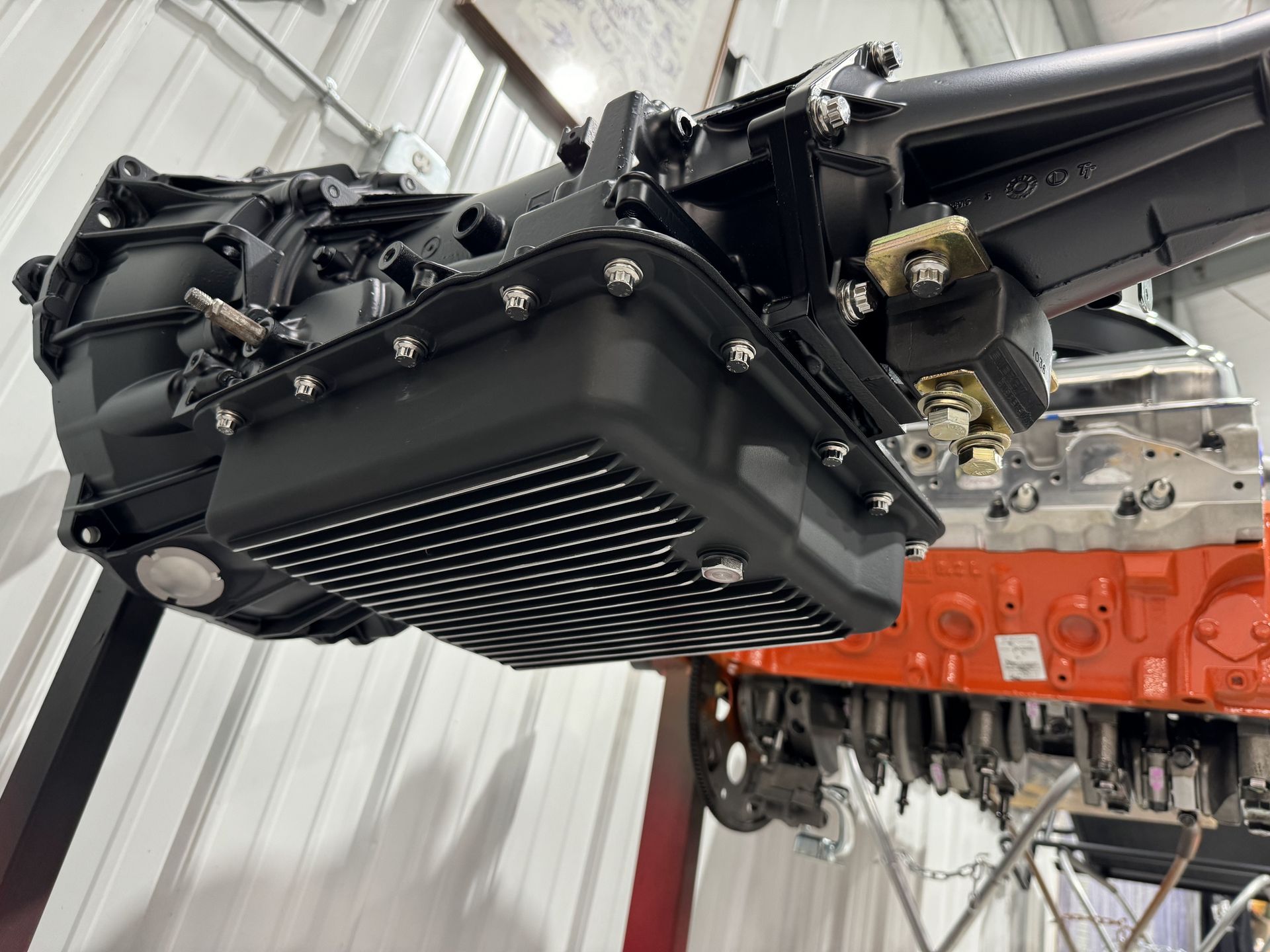 Black automotive component mounted beneath an orange vehicle chassis in a workshop