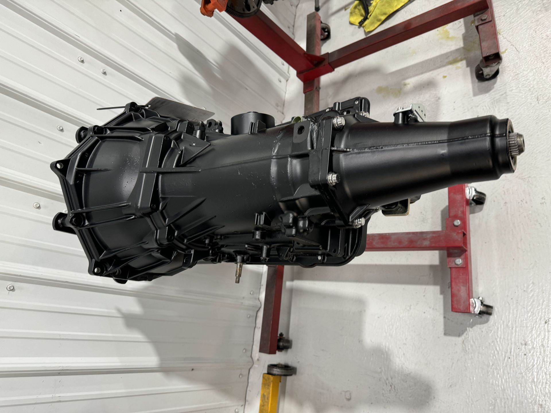 Black automotive transmission on a lift in a garage with white walls and red support stands