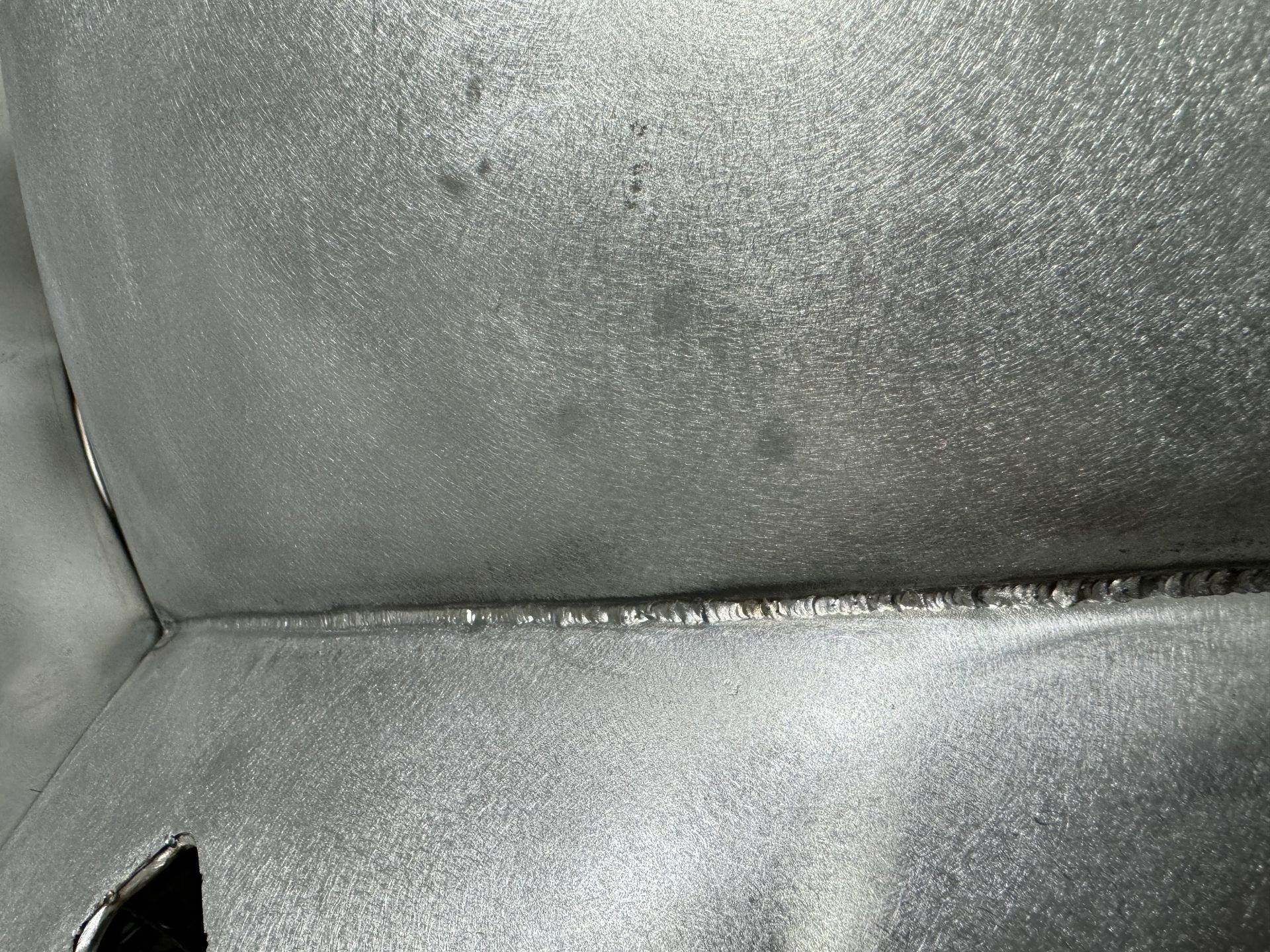 Close-up of gray, textured upholstery with a seam and a small tear at the lower left.