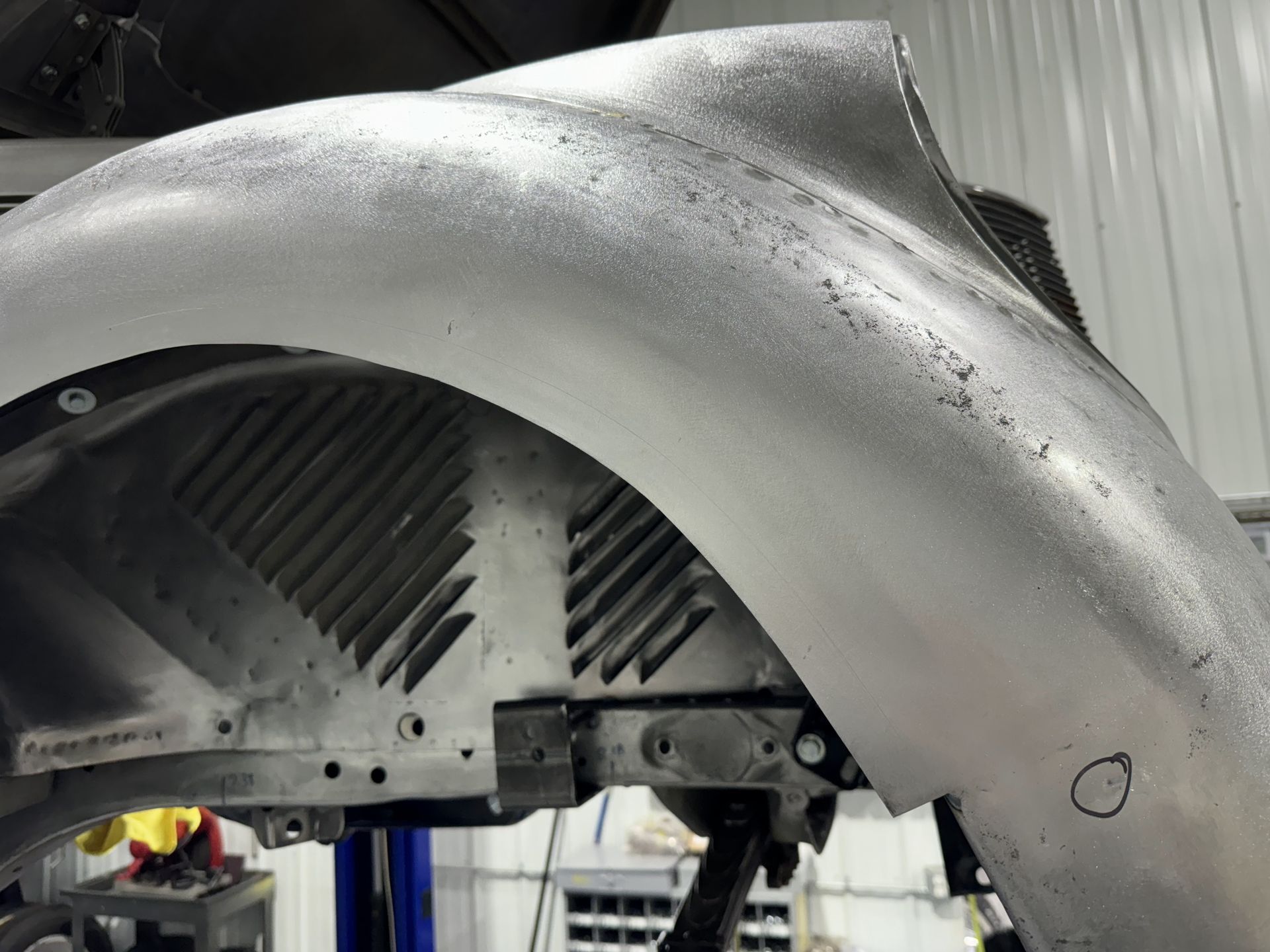 Close-up of a silver car fender in a workshop, showing exposed inner paneling and fasteners.