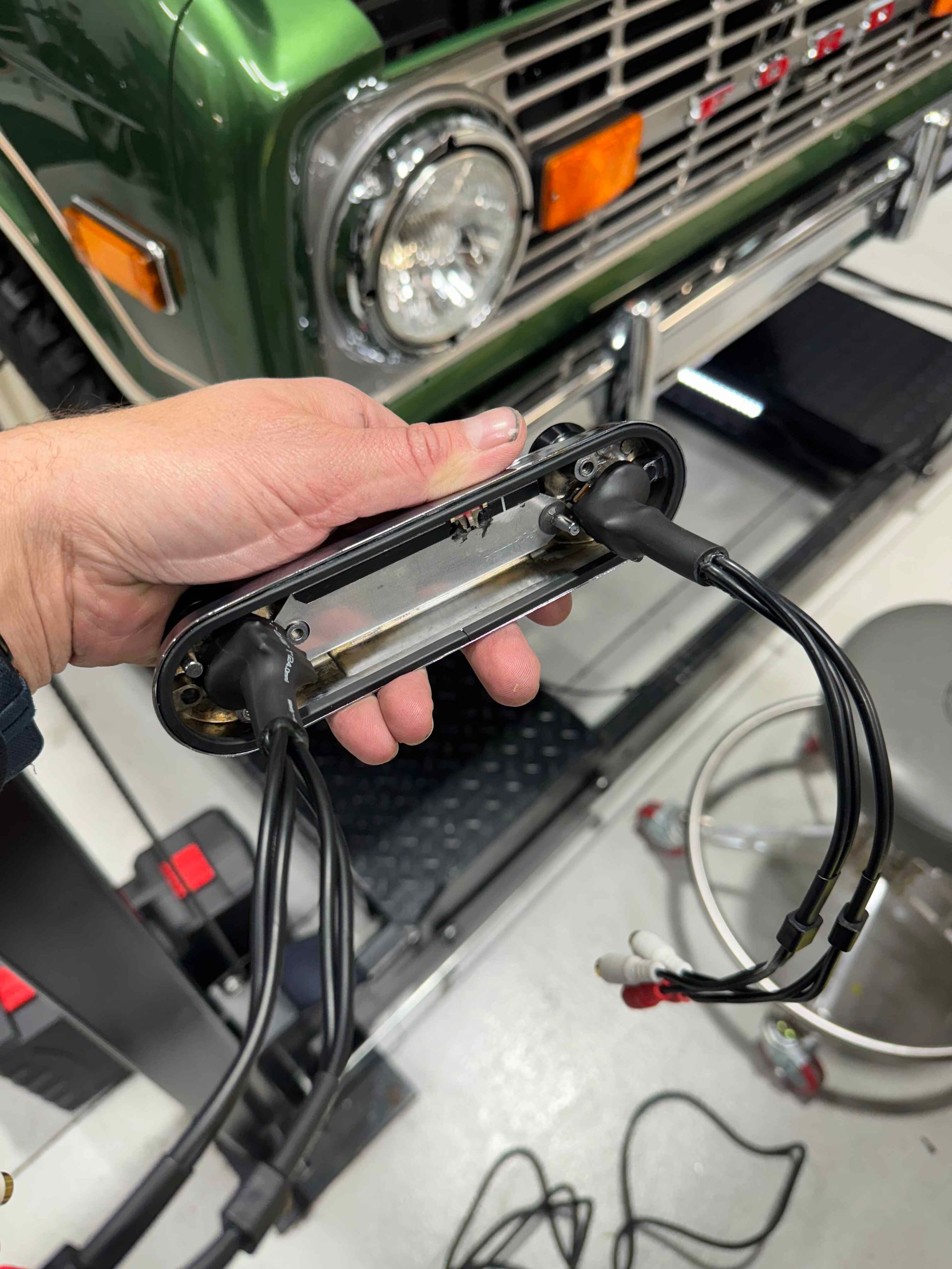 Hand holding a black cable tie and wire harness in front of a green vintage vehicle grille