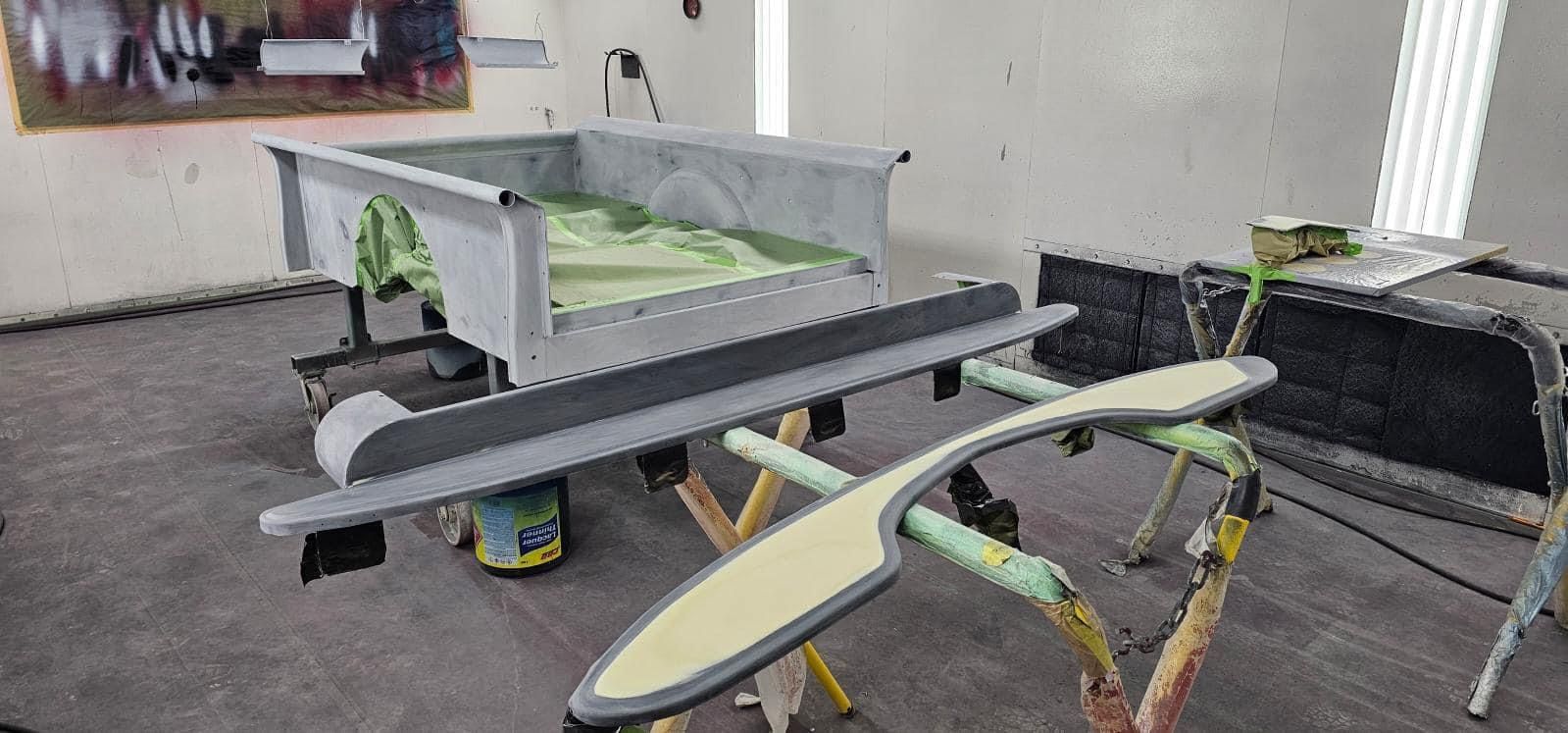 Indoor workshop with a model airplane on a stand, alongside another wing section and a long gray panel.