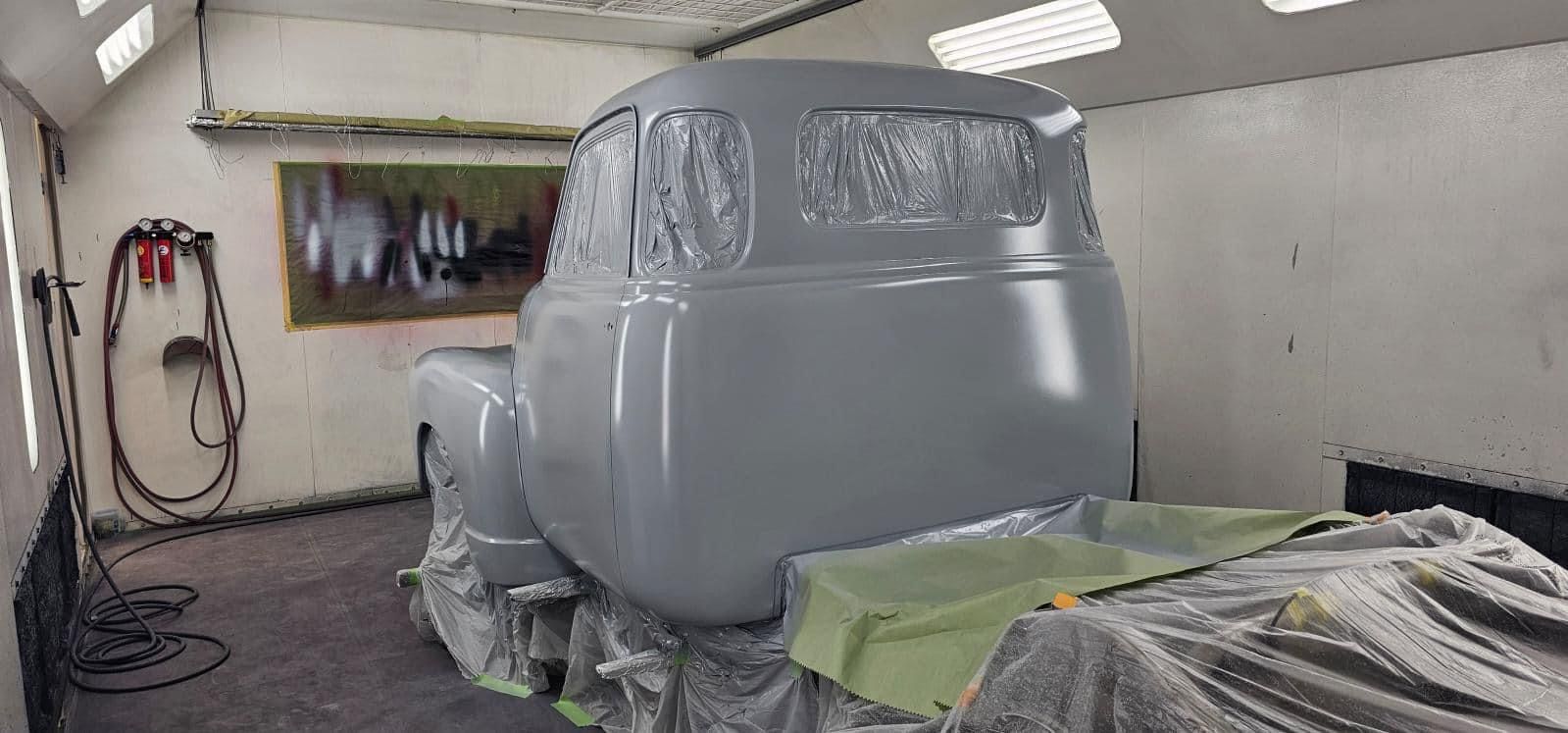 Silver car body in a paint booth, masked and covered for spray painting
