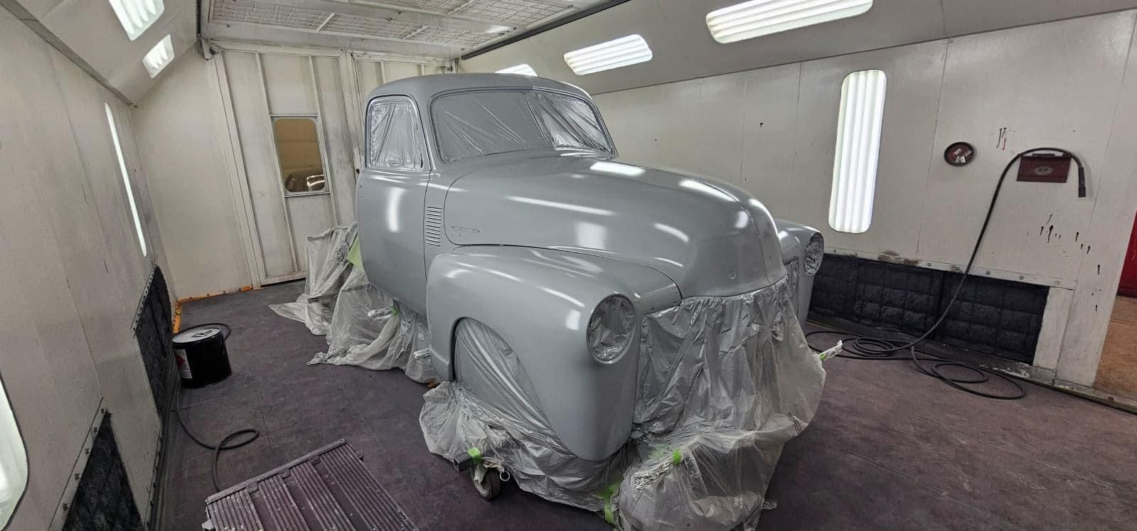 Gray classic car covered in masking plastic inside an auto body shop, awaiting paint.