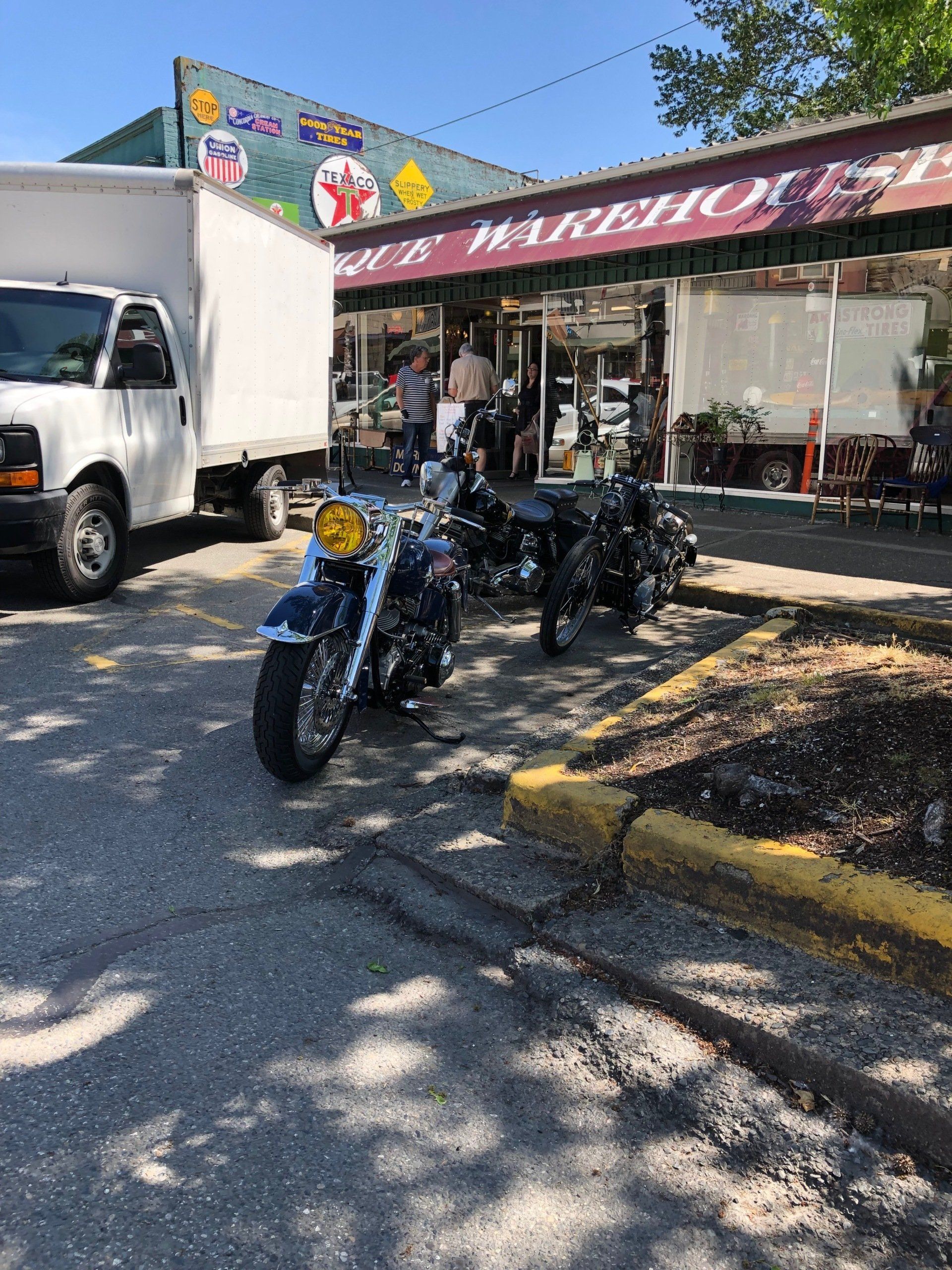 Motorcycle parked outside a storefront with a truck beside it on a sunny day