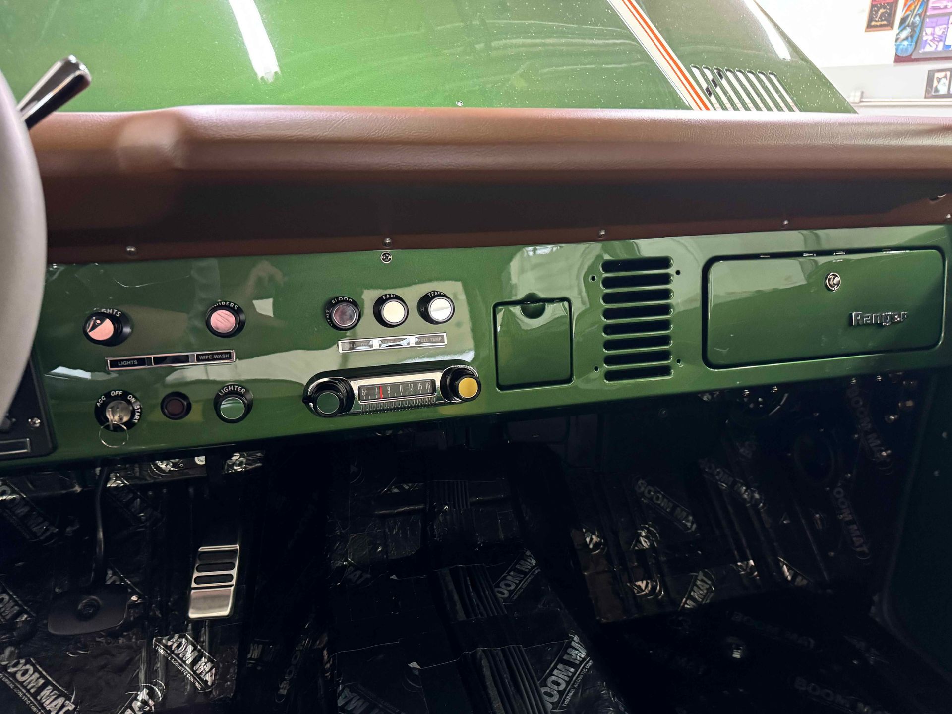 Green vehicle dashboard with switches, gauges, vents, and a storage compartment under the windshield