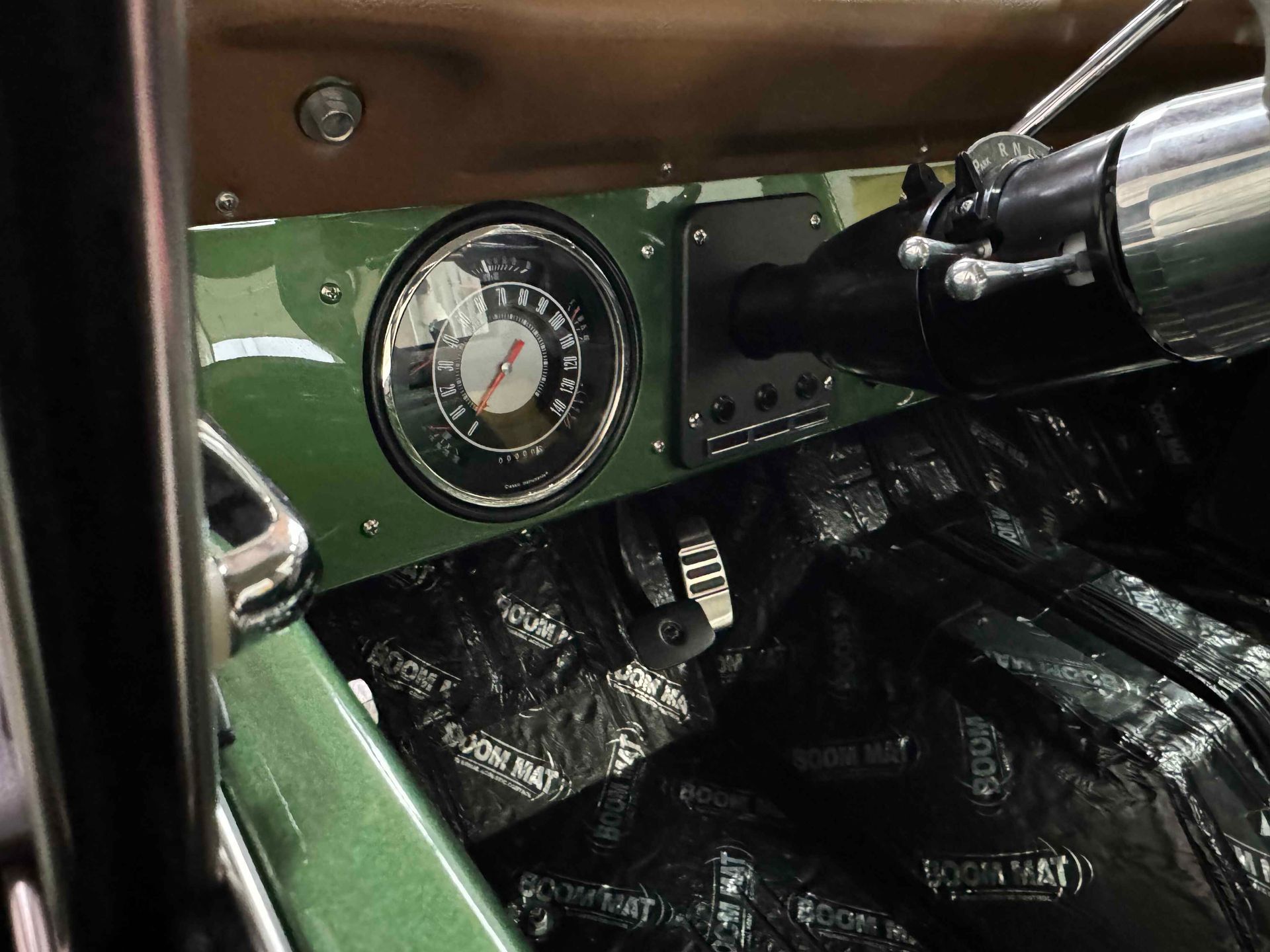 Vintage car dashboard with green panel, round gauge, and chrome controls over black interior upholstery