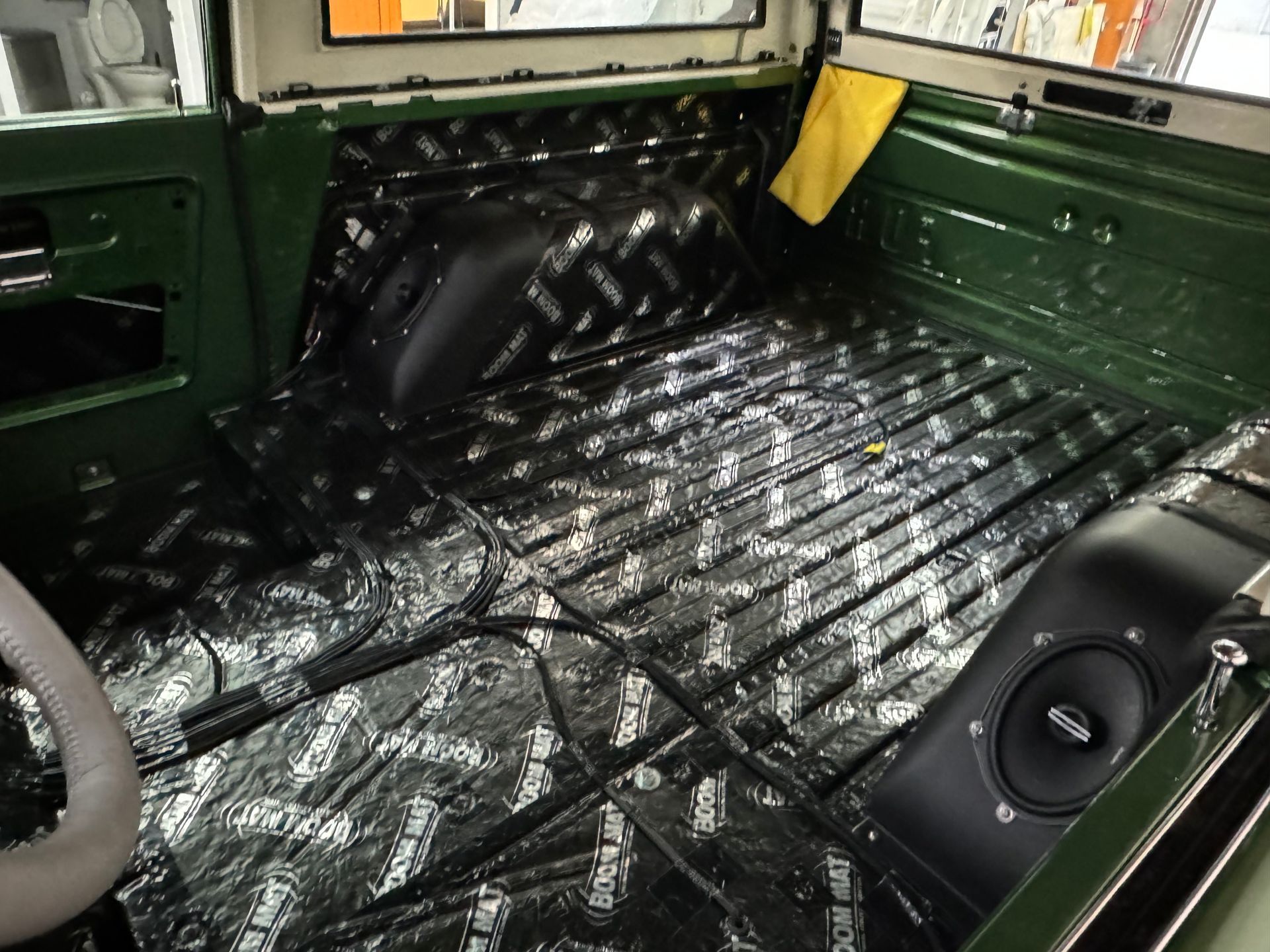 Green vehicle cargo area with black bed liner and rolled-up white mat on the floor