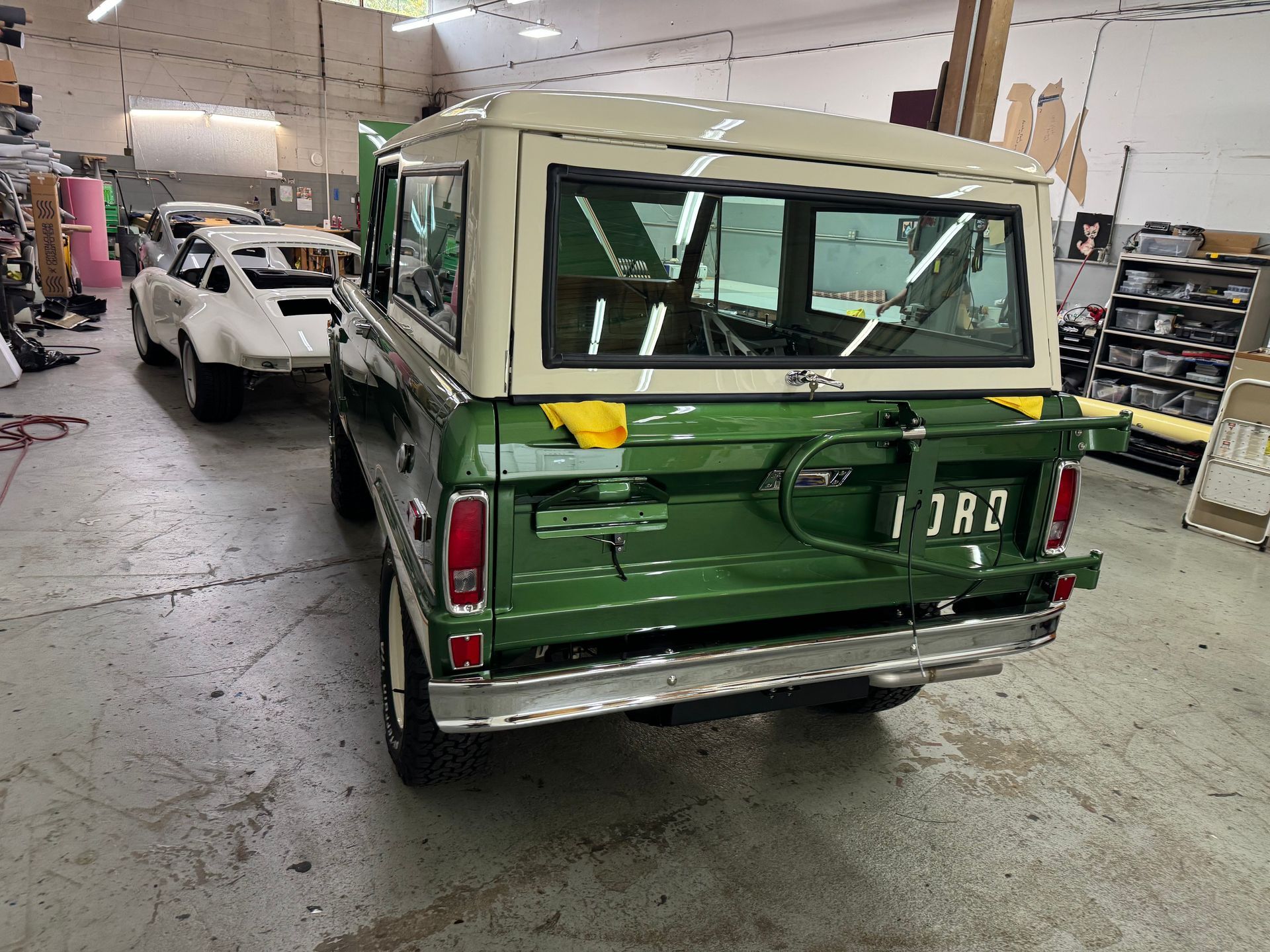 Classic green-and-cream SUV in an auto shop, rear view with a white car nearby.