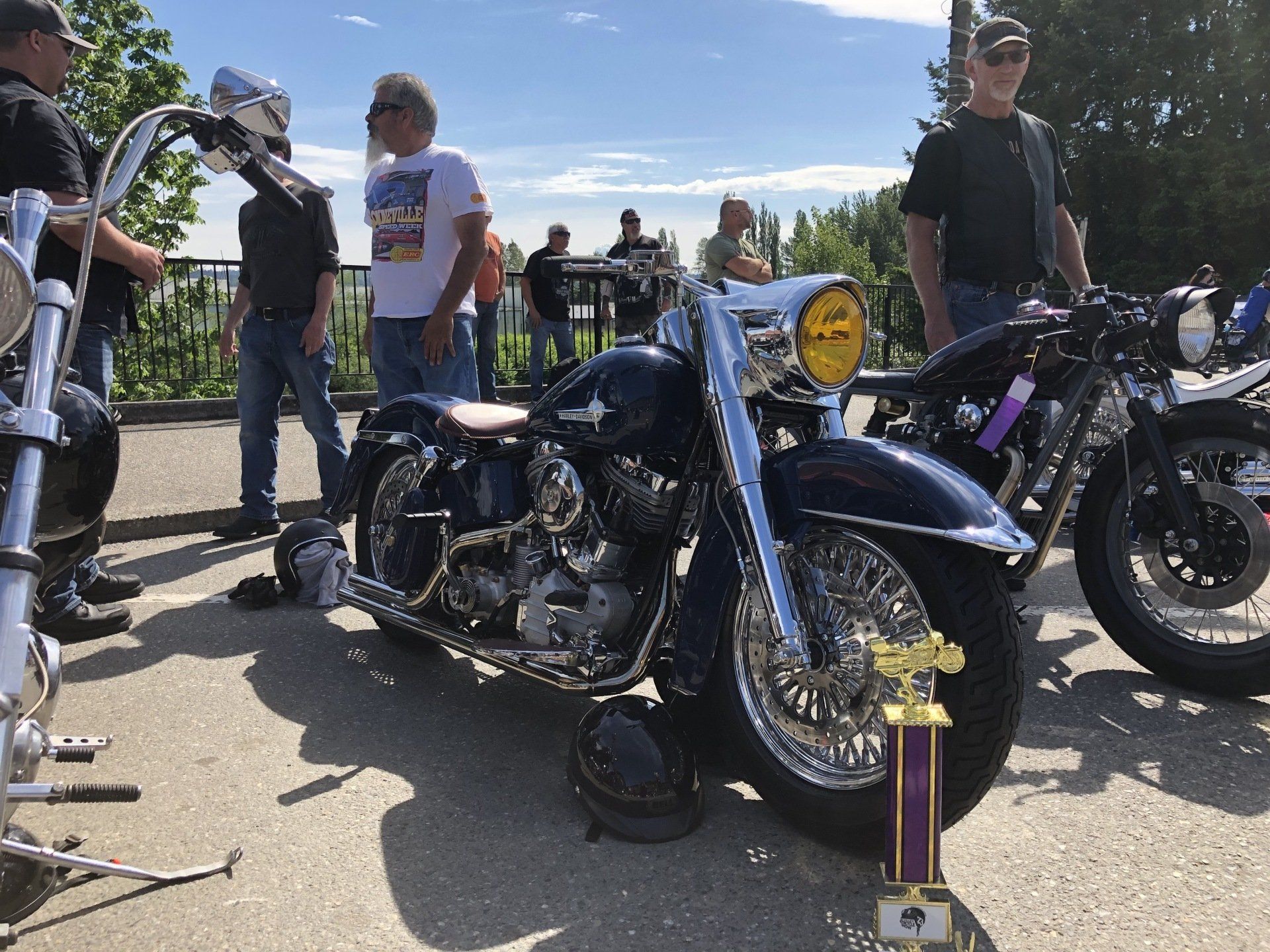 Motorcycle show with a black cruiser and trophy in front, people standing nearby outdoors