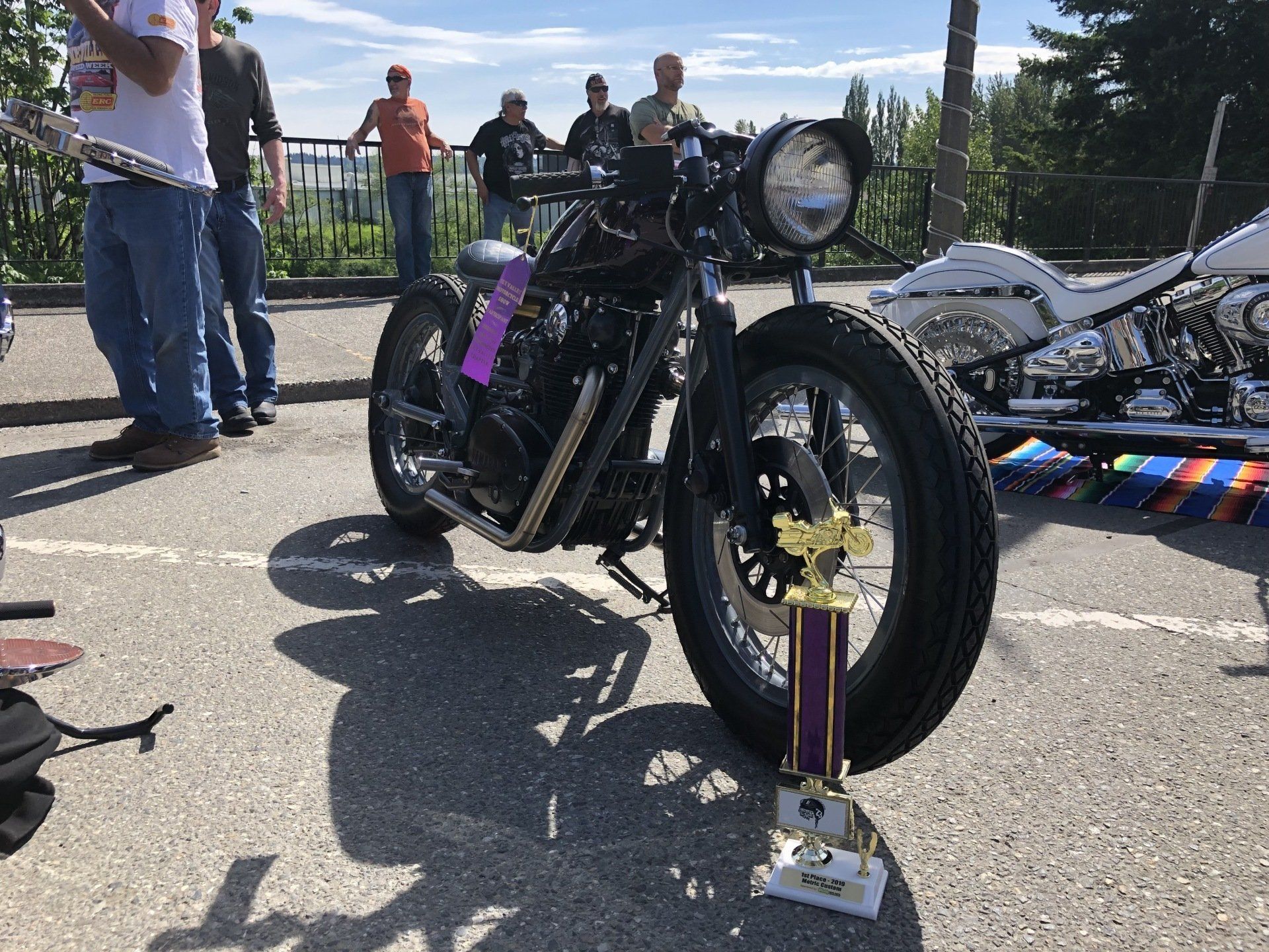 Black vintage motorcycle with purple ribbon and trophy on display outdoors at a car show