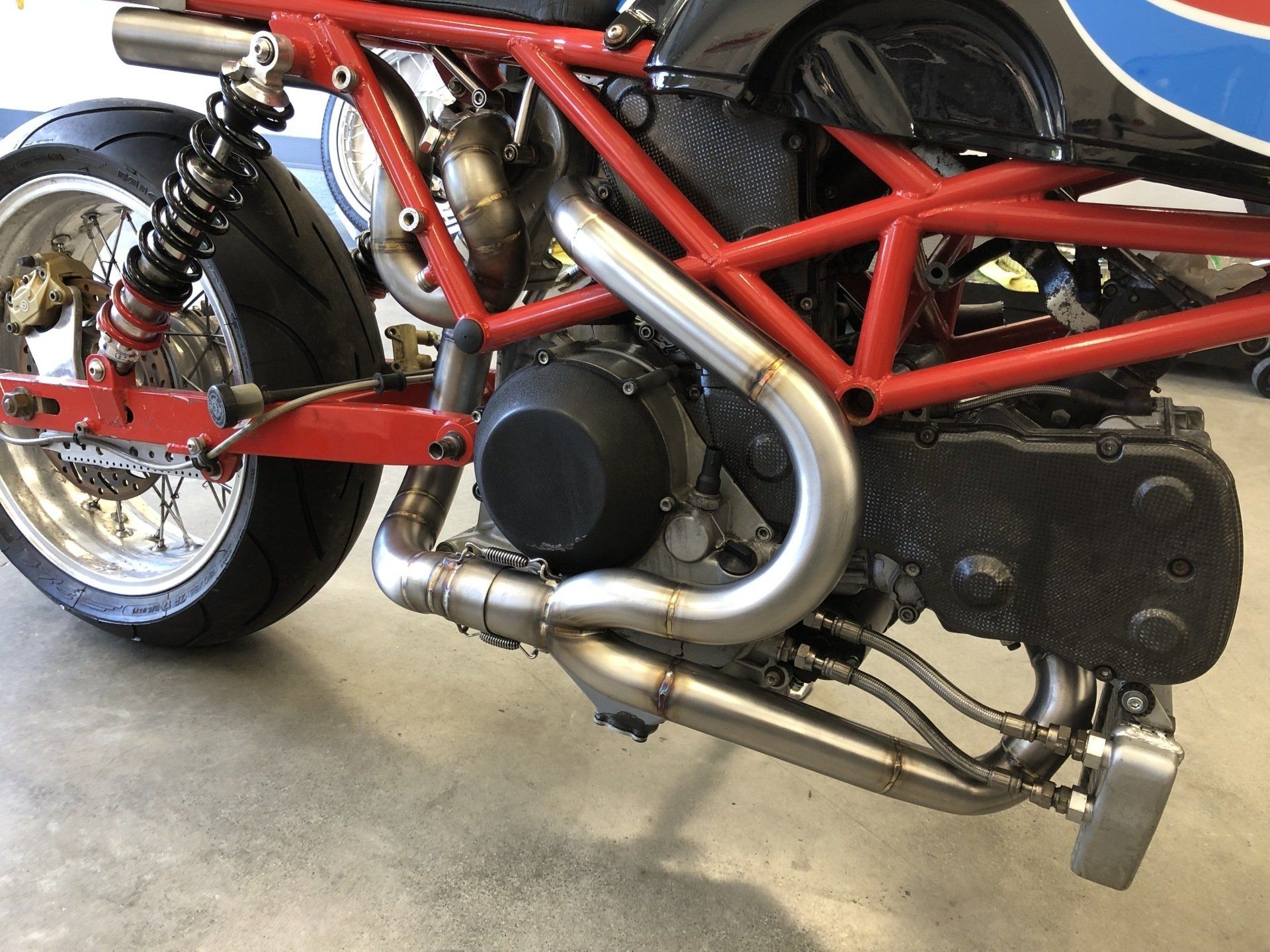 Red-framed motorcycle with exposed engine and chrome exhaust on a garage floor.