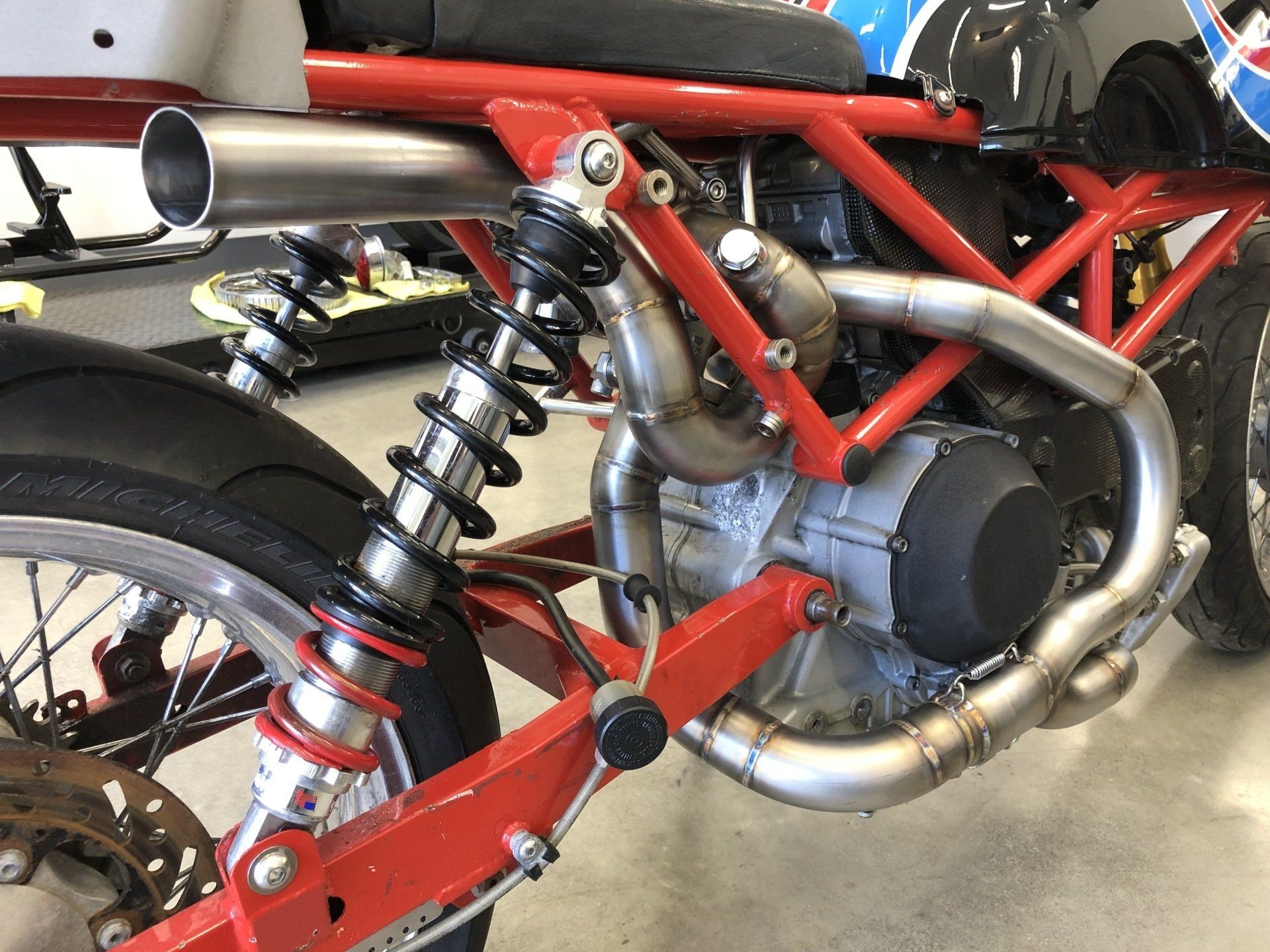 Red motorcycle frame with exposed engine, rear suspension, and large silver exhaust pipe.