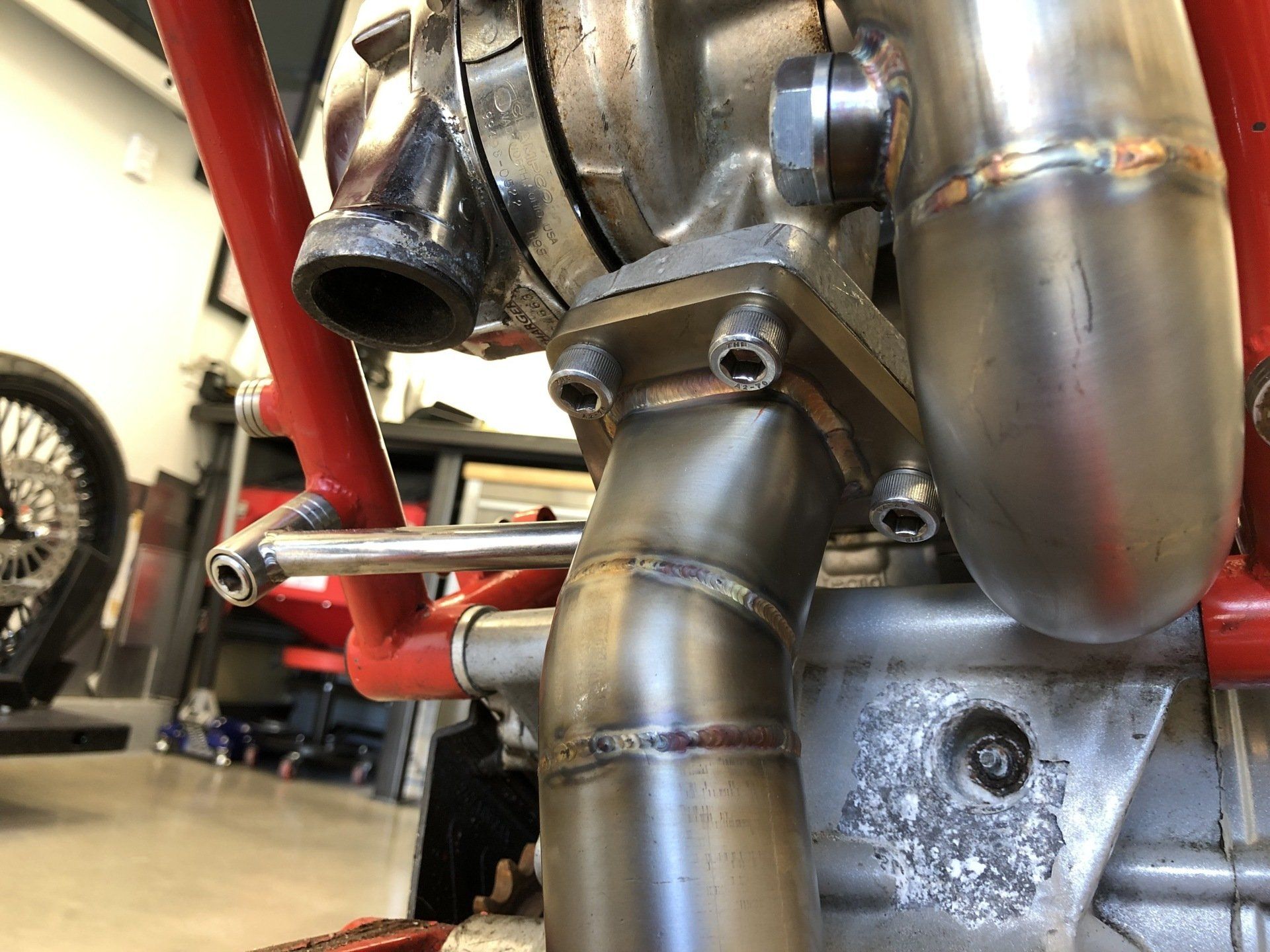 Close-up of a shiny motorcycle engine and exhaust pipes with a red frame in a garage.