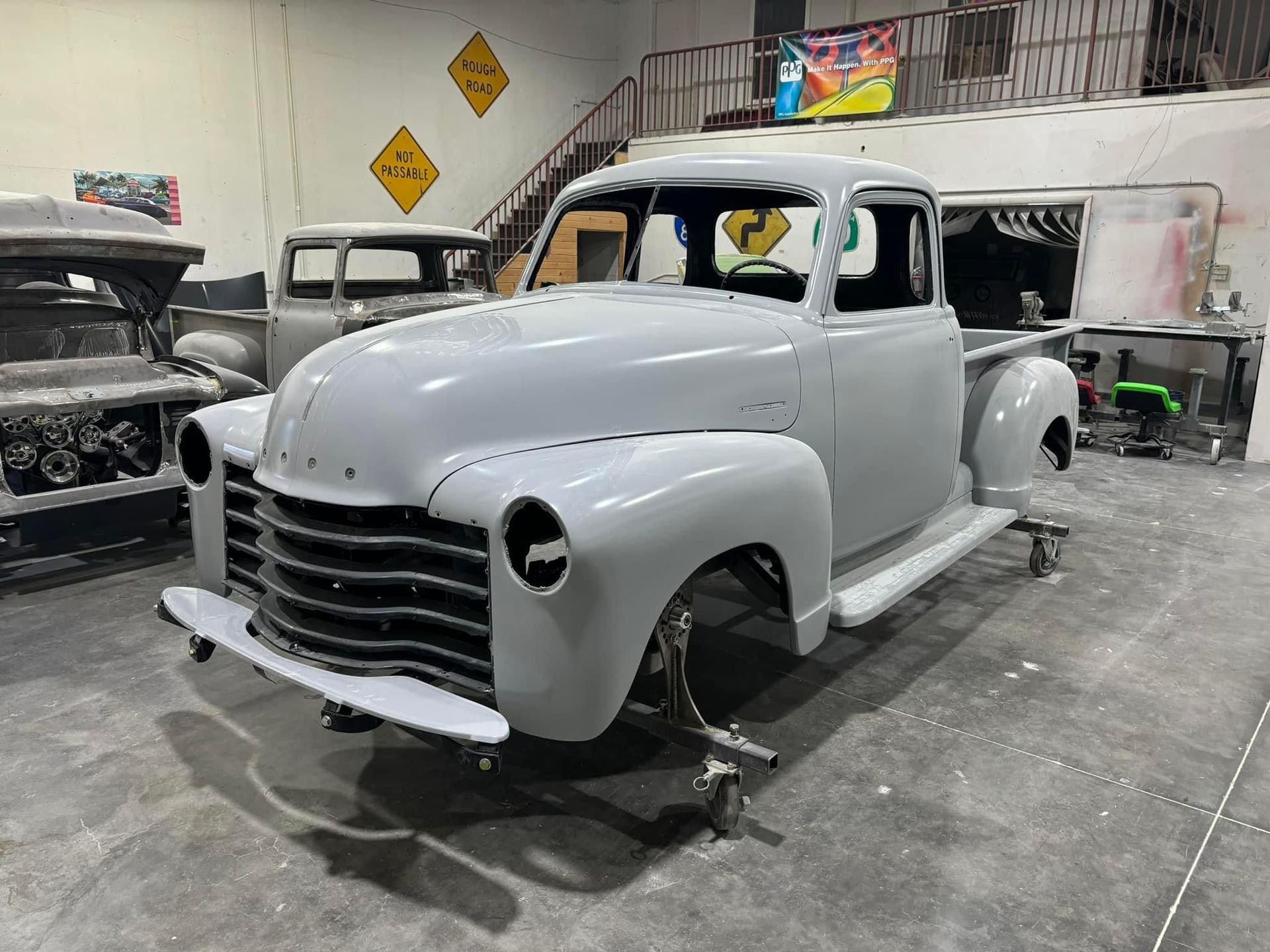 Primer gray vintage pickup truck in an auto shop, missing wheels and front trim, under restoration