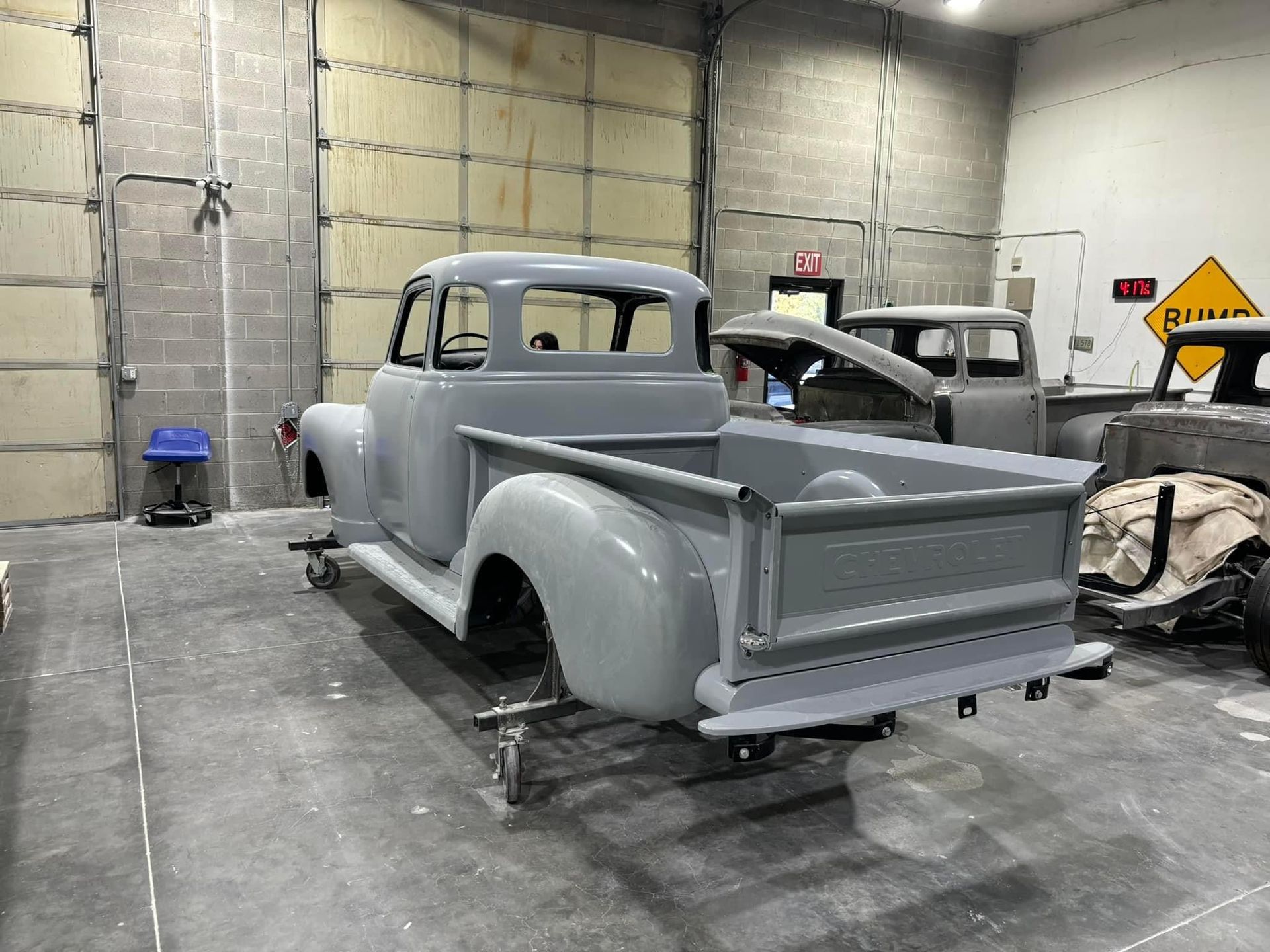 Classic gray pickup truck undergoing restoration in a garage with concrete block walls.