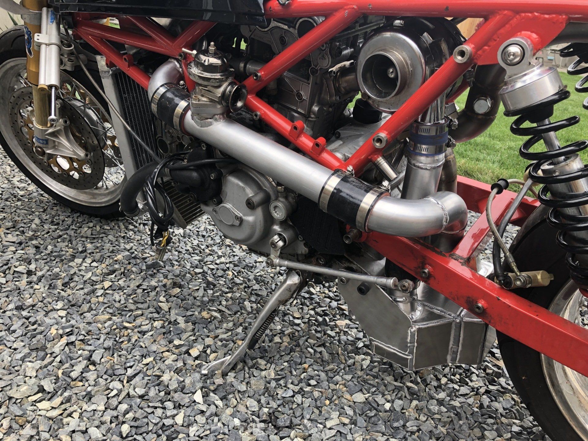 Close-up of a red motorcycle engine and exhaust with black frame on gravel.