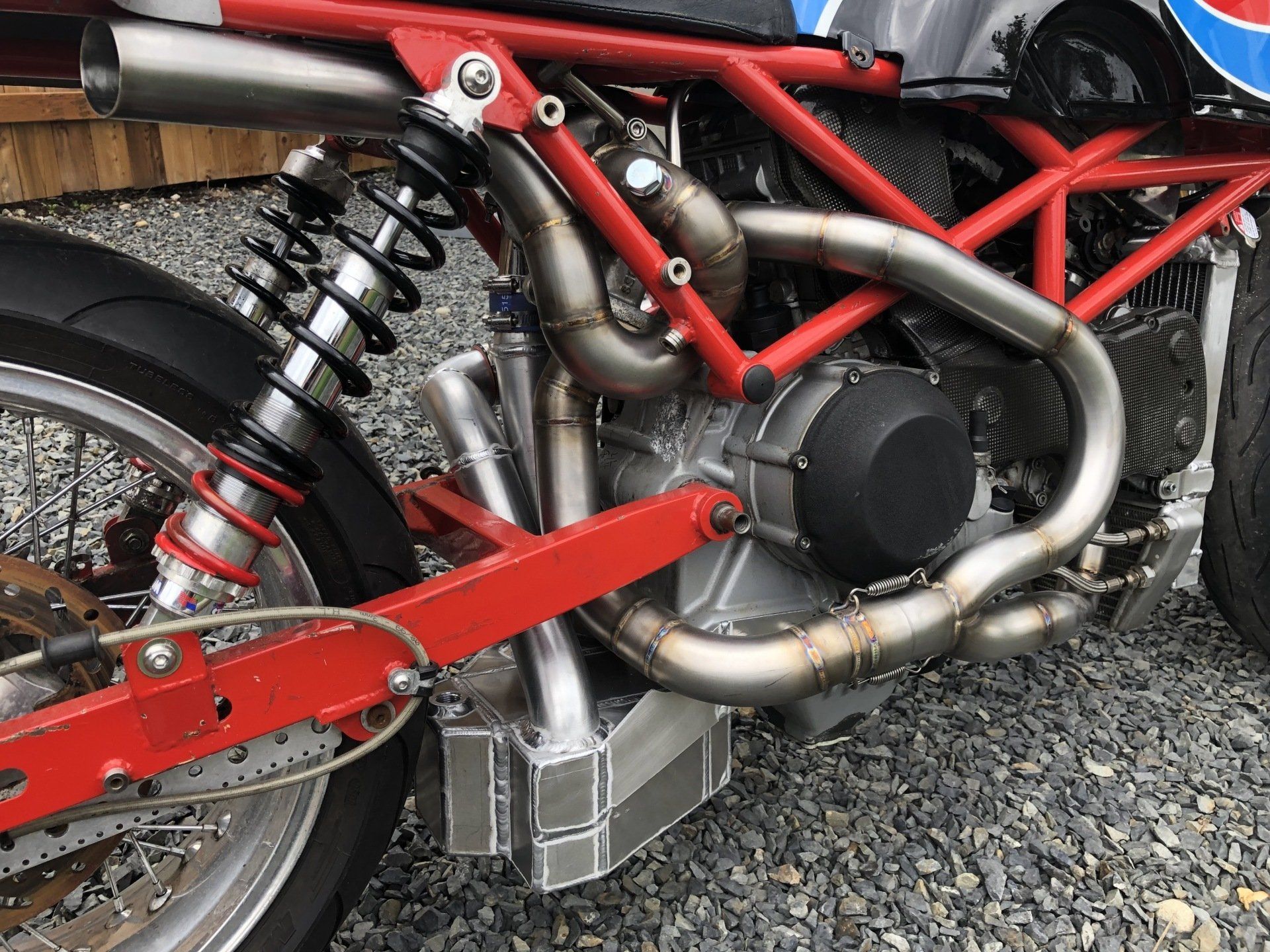Close-up of a red motorcycle frame and rear suspension with exposed engine and exhaust pipes