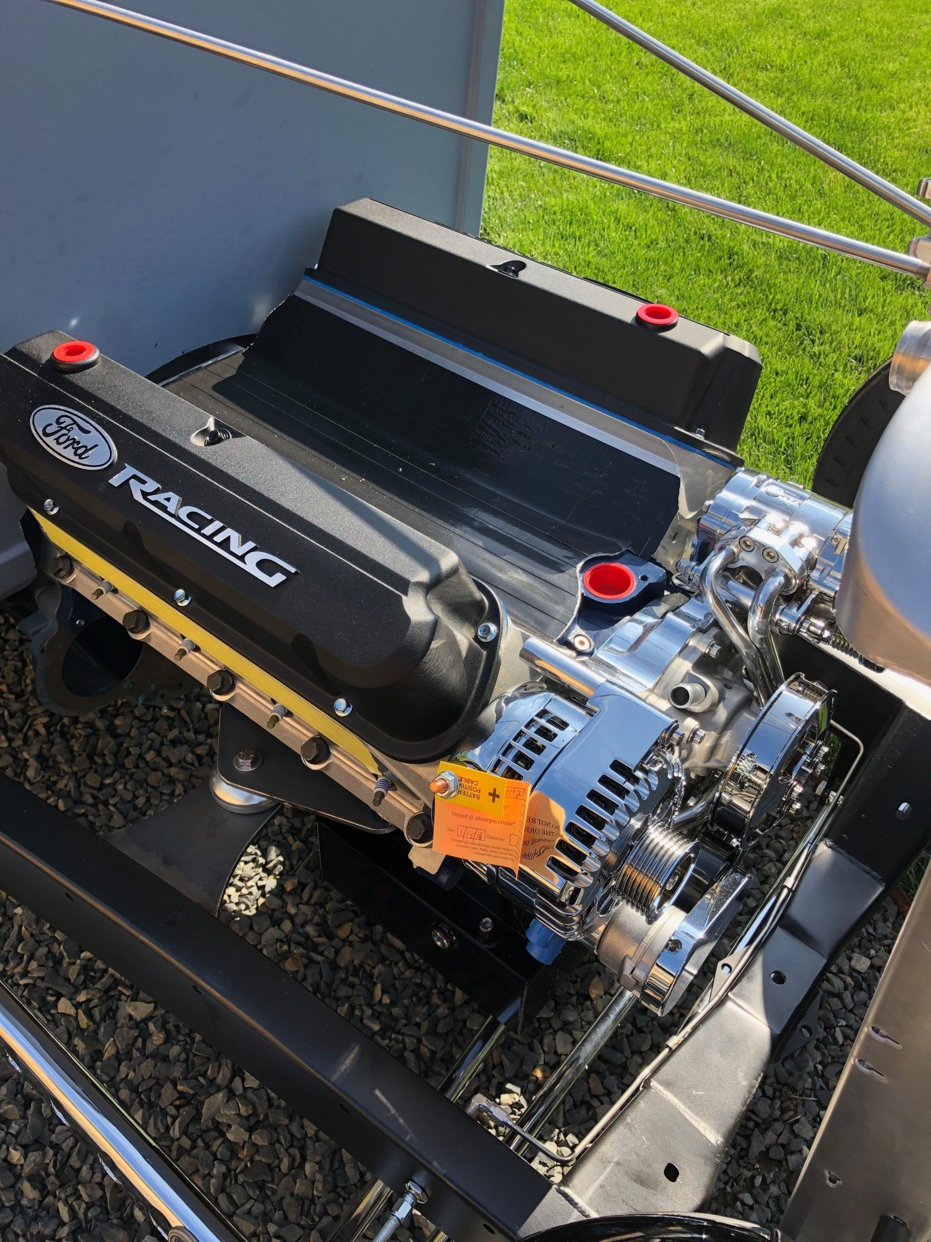 Small RC car engine on a display stand outdoors, with chrome parts and black Racing branding.
