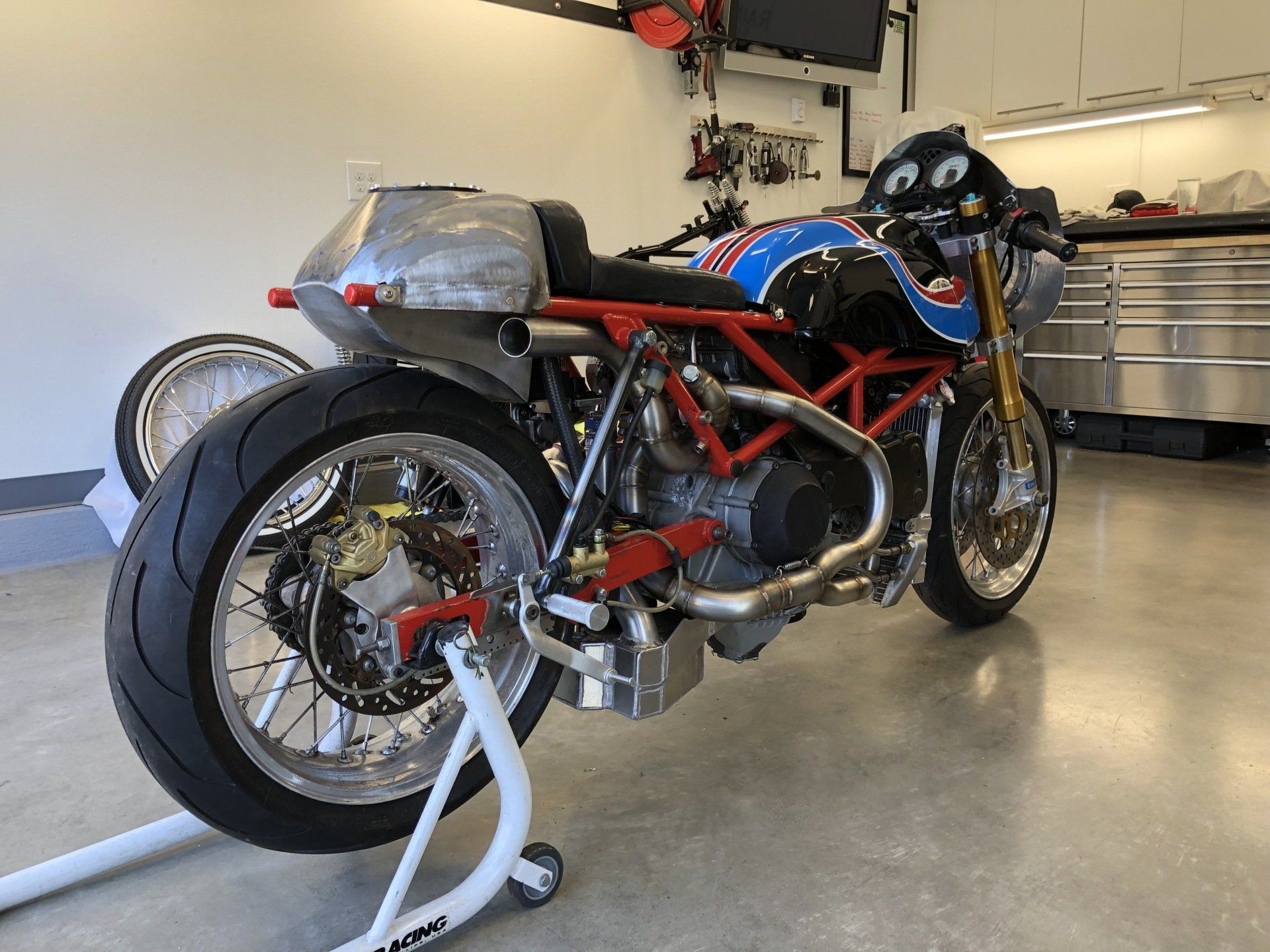 Red sport motorcycle on a stand in a garage, with exposed red frame and rear wheel visible.