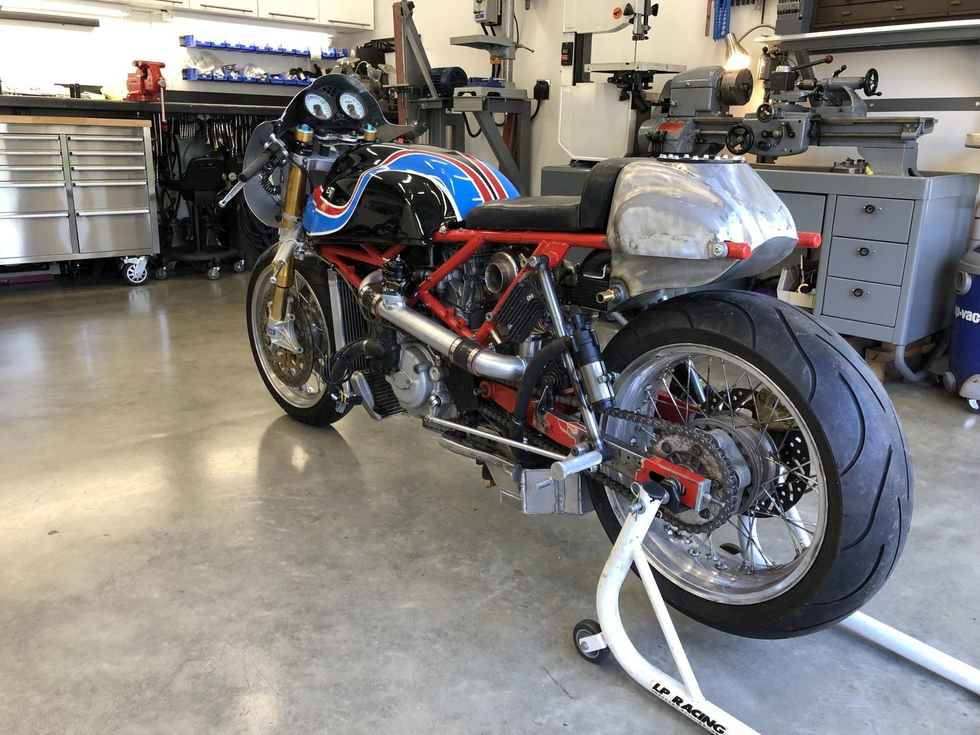 Racing motorcycle with blue and red fairings in a garage, parked on a rear stand.