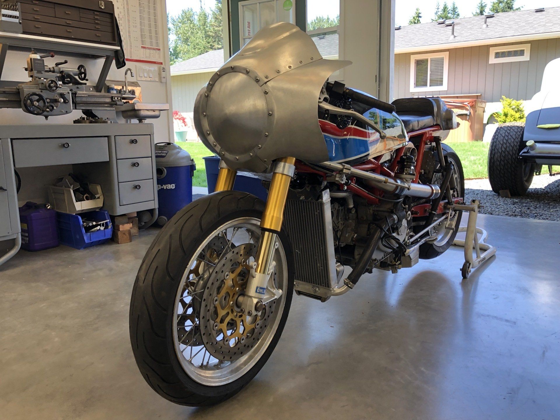 Custom racing motorcycle in a garage, showing a silver fairing, gold forks, and chrome front wheel.