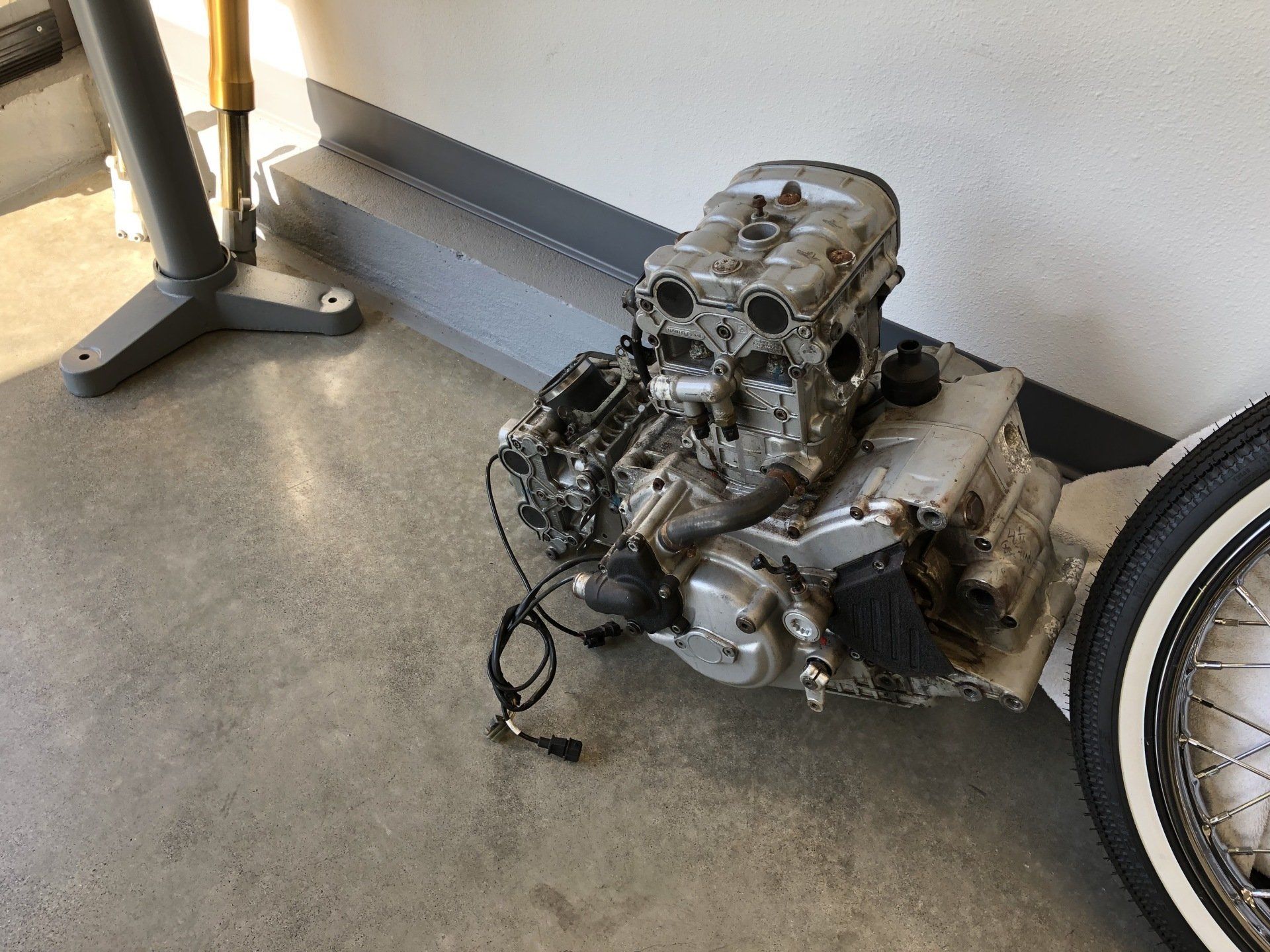 Engine on the floor beside a bicycle wheel in a garage or workshop