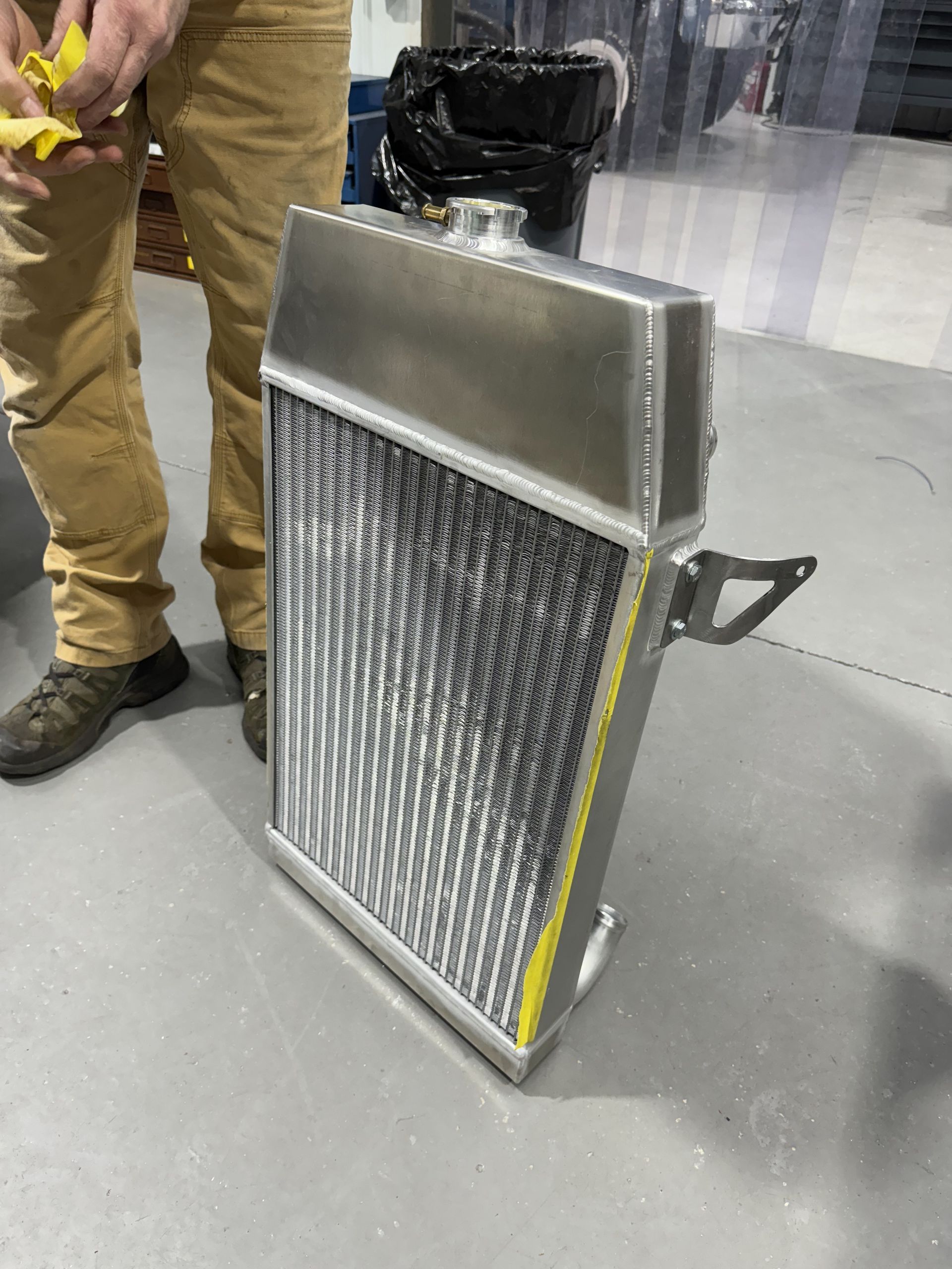 Metal radiator/heat exchanger standing on a gray floor beside a person in tan pants and boots.