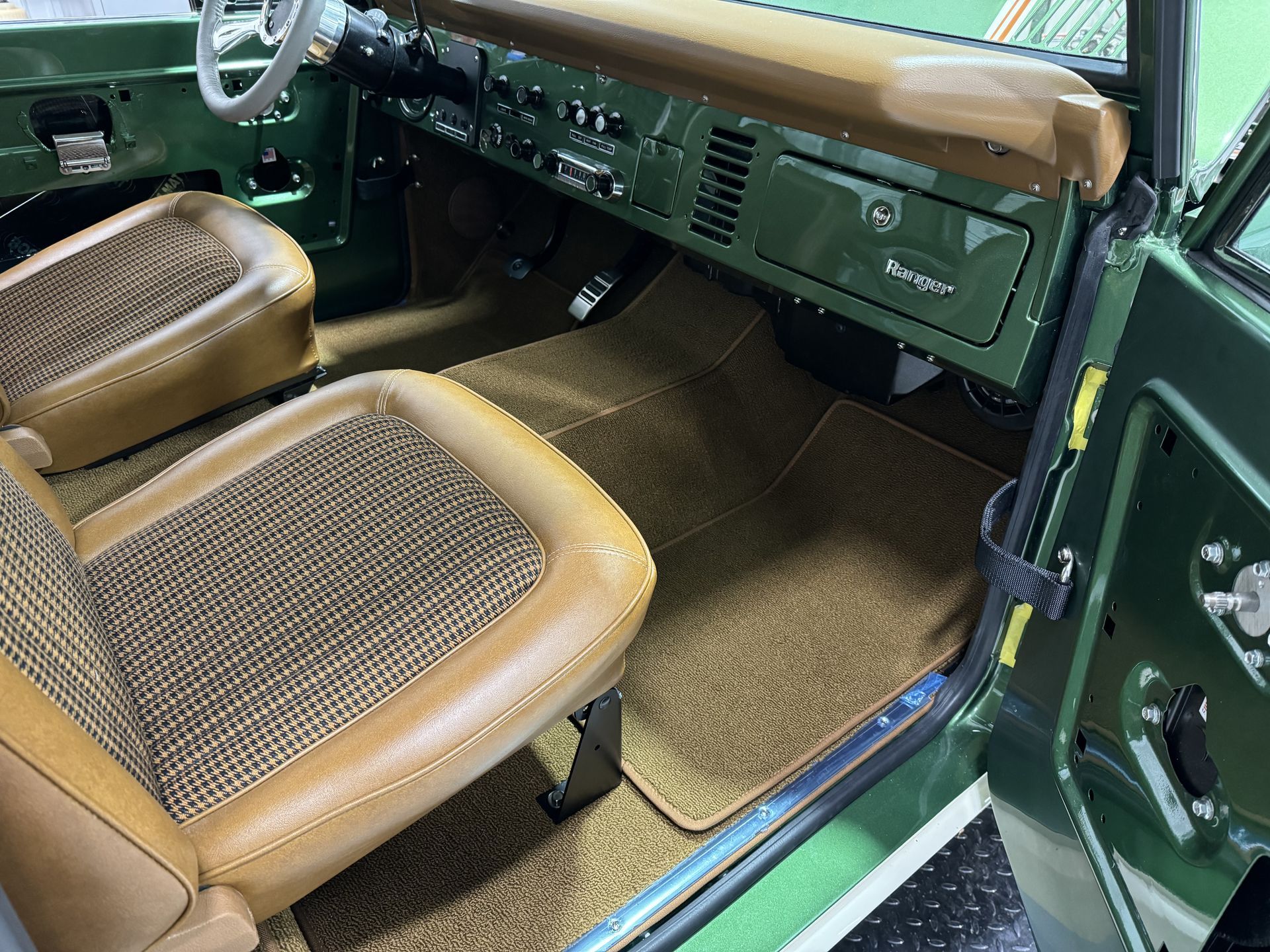 Classic car interior with green dashboard, tan seats, and open passenger door