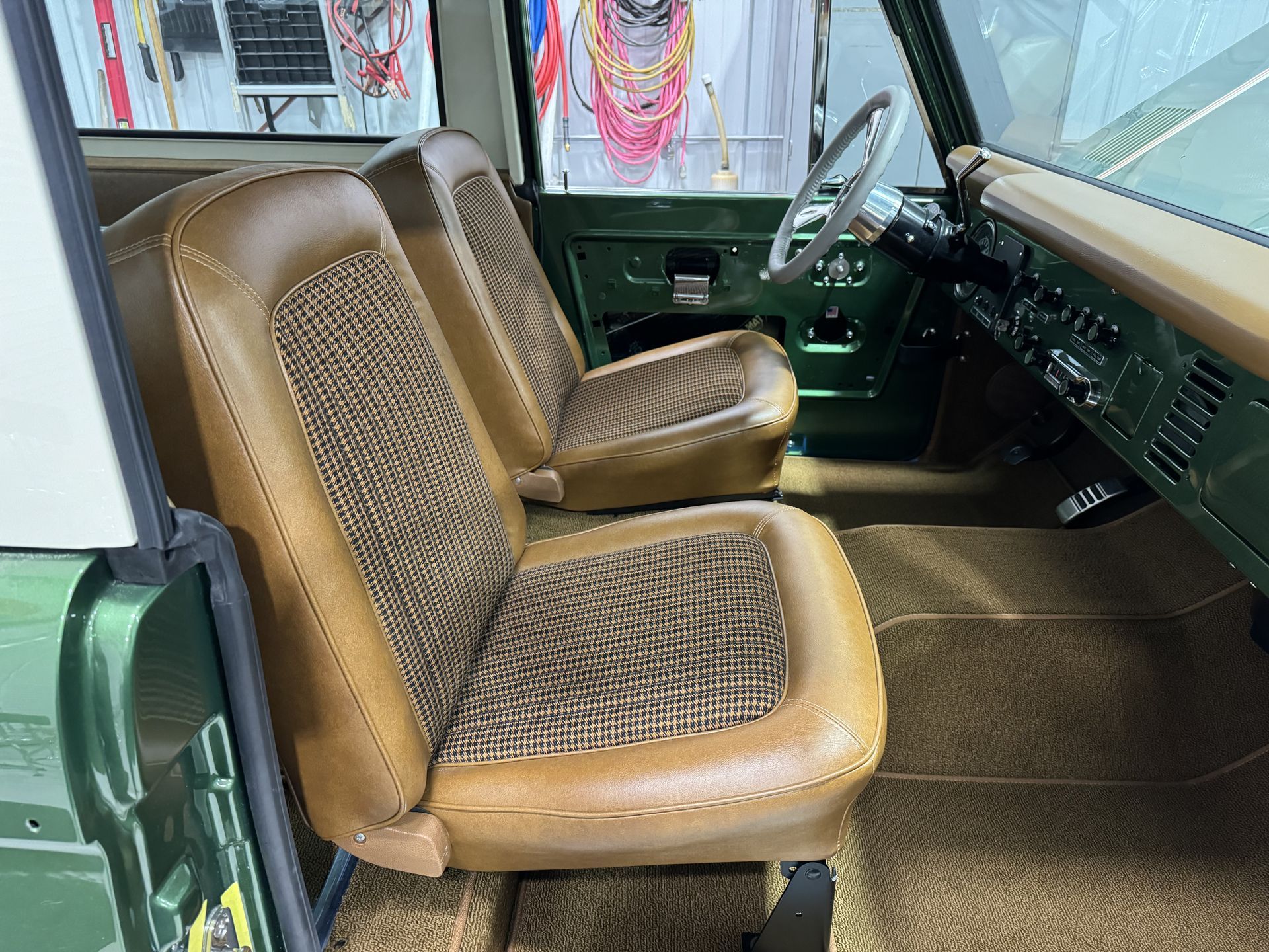 Green vintage car interior with tan patterned front seats and dashboard, viewed from the passenger side