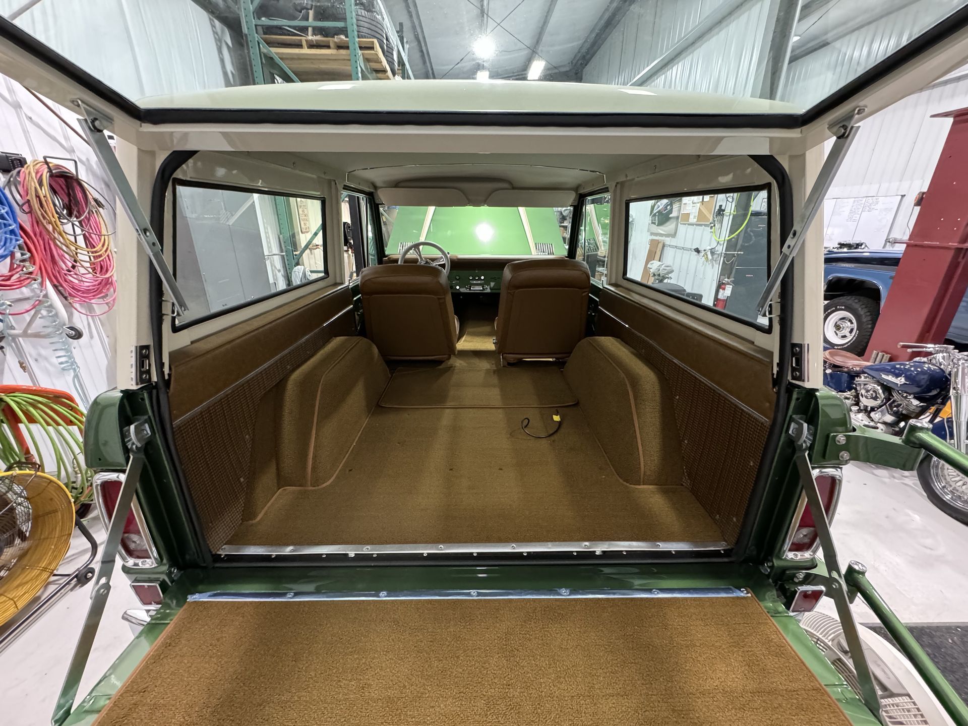 Interior of a vintage vehicle with tan upholstery and a green body, viewed from the open rear hatch in a garage.