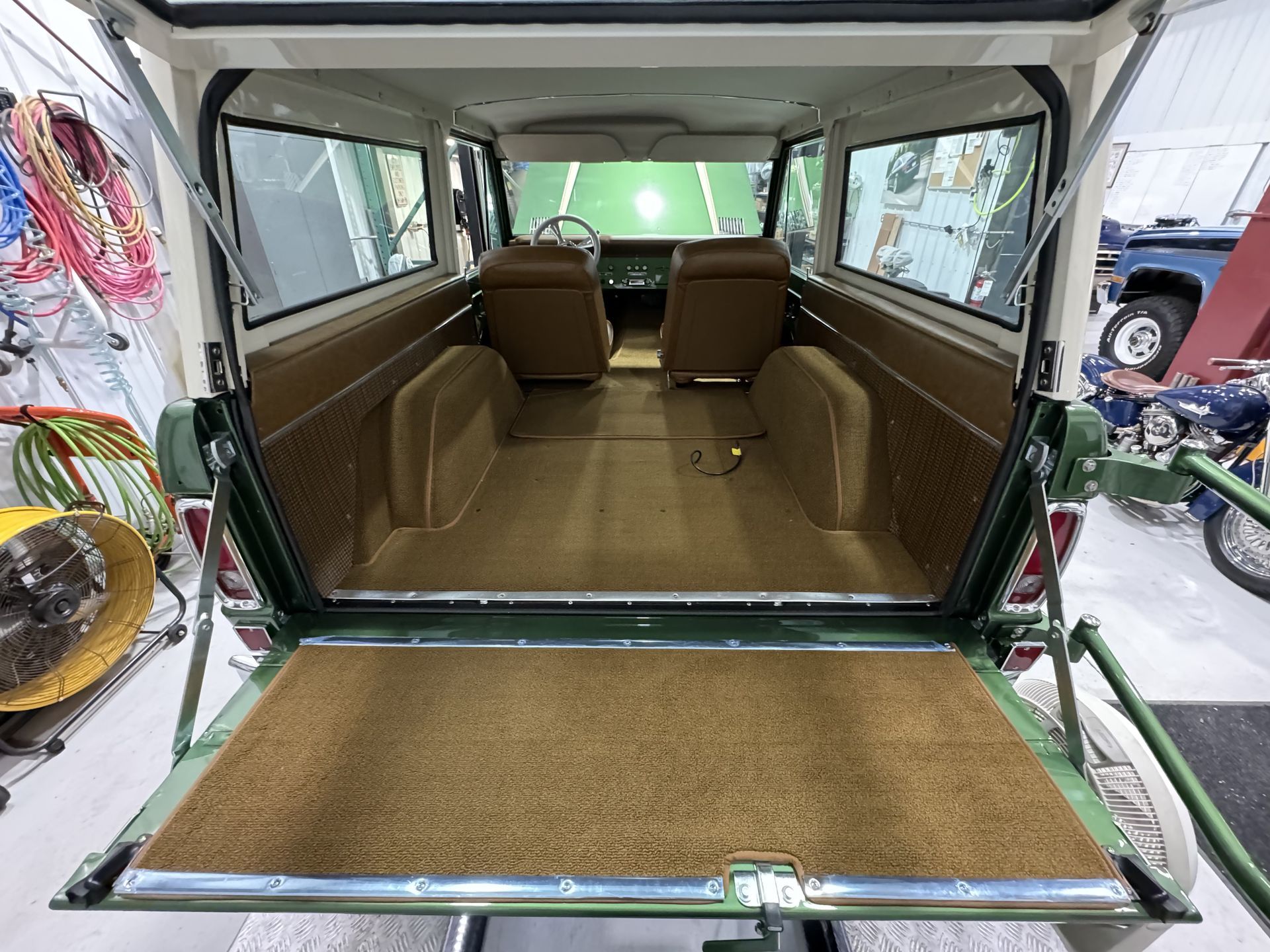 Open rear of a green vehicle showing a tan interior cargo area and rear seats.